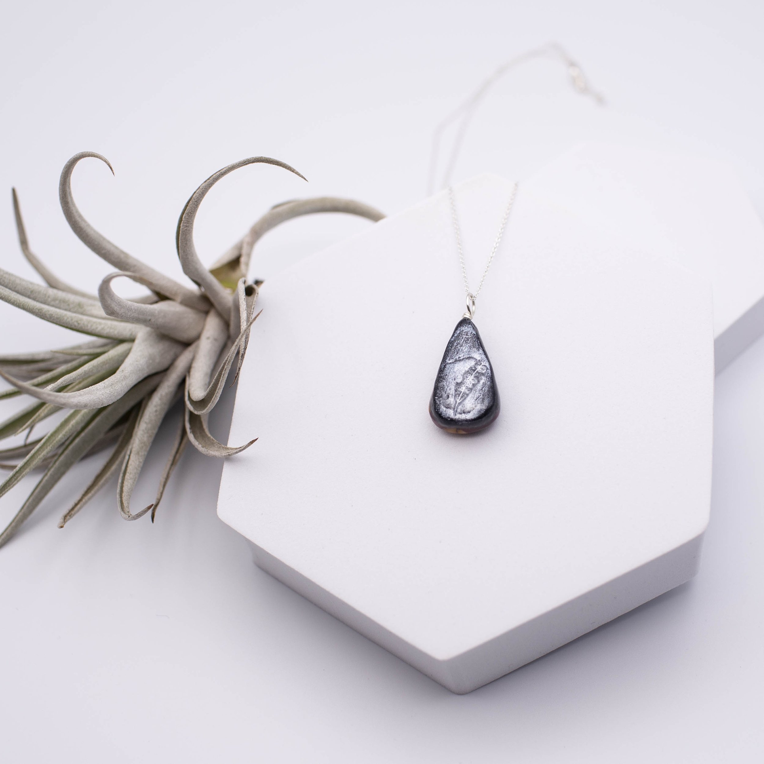 Warm red/burgundy and yellow color mookaite jasper gemstone pendant with a black apoxie sculpt leaf design with pearl pigment powder on the back silver chain necklace.