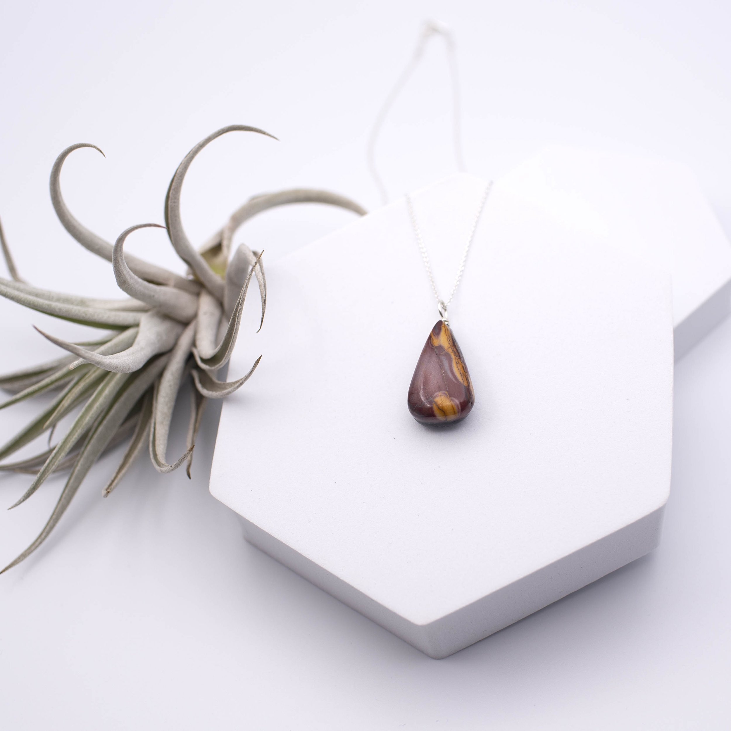 Warm red/burgundy and yellow color mookaite jasper gemstone pendant with a black apoxie sculpt leaf design with pearl pigment powder on the back silver chain necklace.