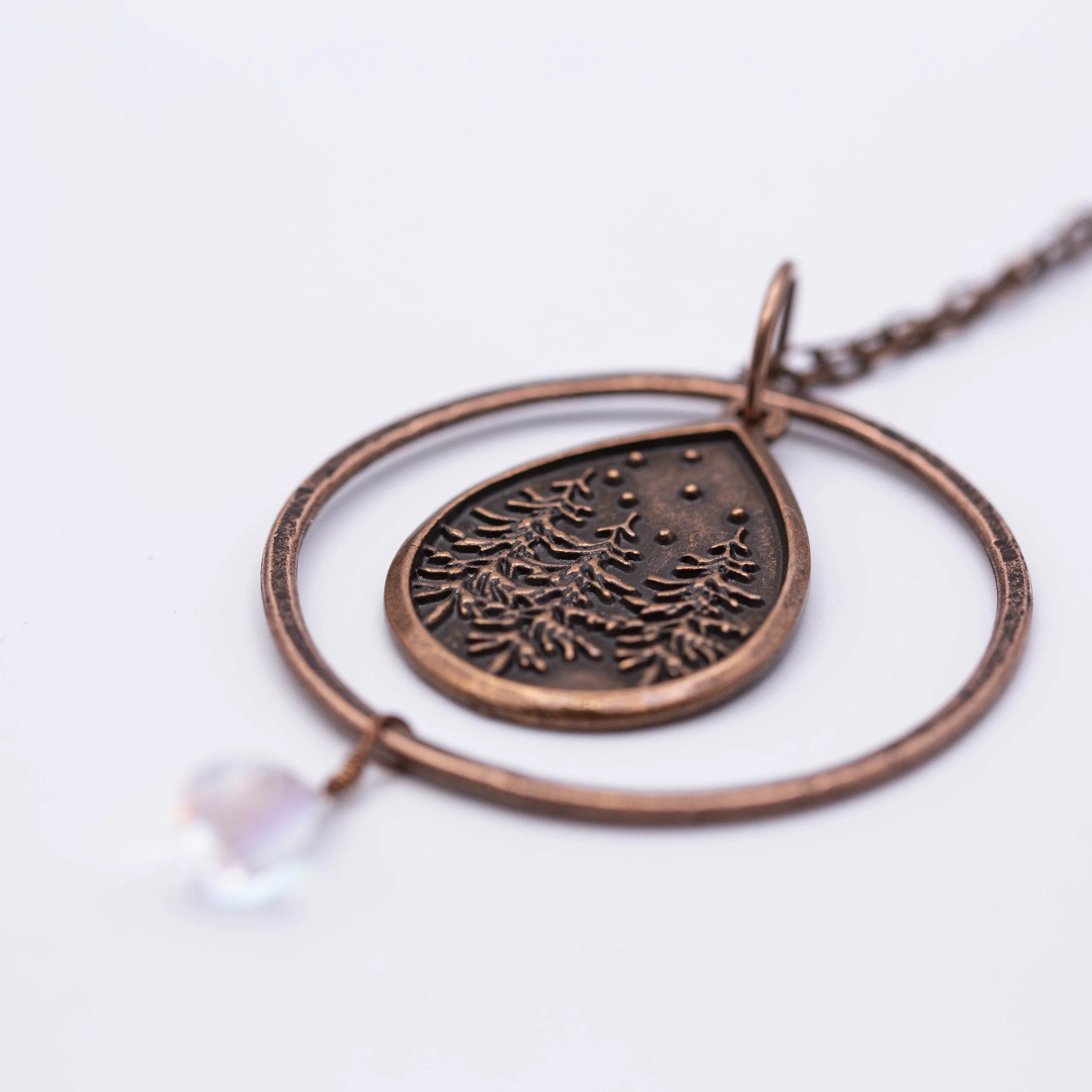 This copper winter pine tree scene teardrop charm sets in a round hoop with a teardrop angel aura flashy quartz gemstone for the perfect winter gift.