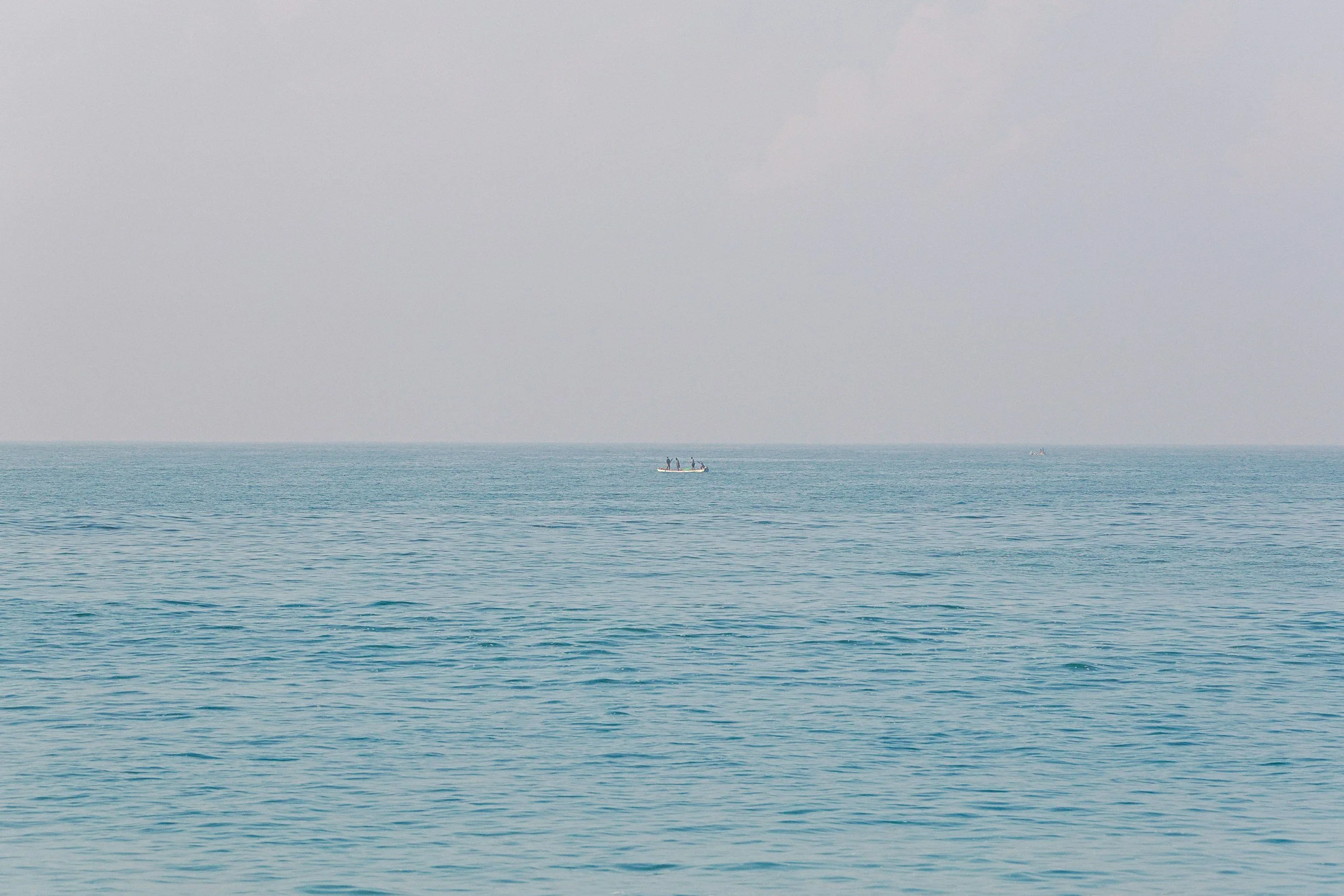 Distant boat with people on calm open sea and hazy sky.