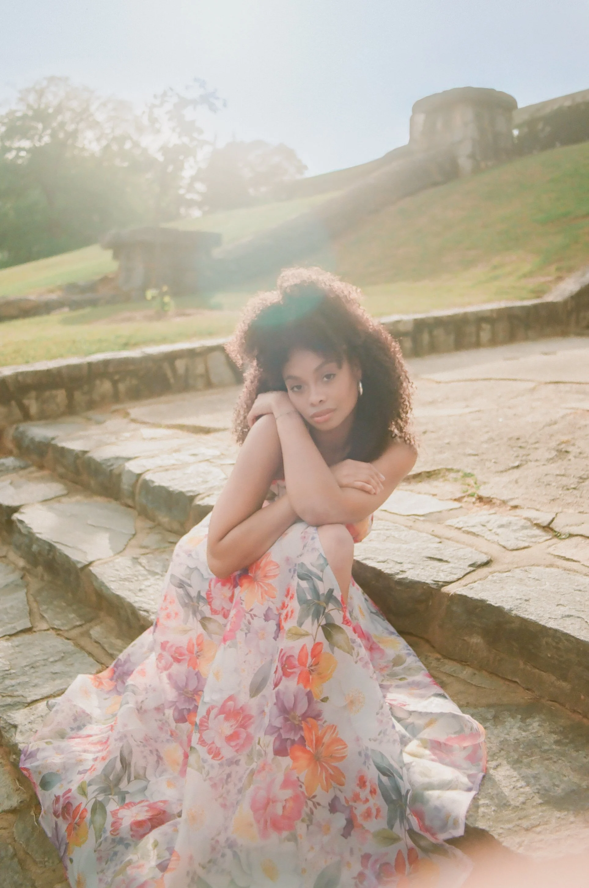 Woman in floral dress sits on stone steps in the day time