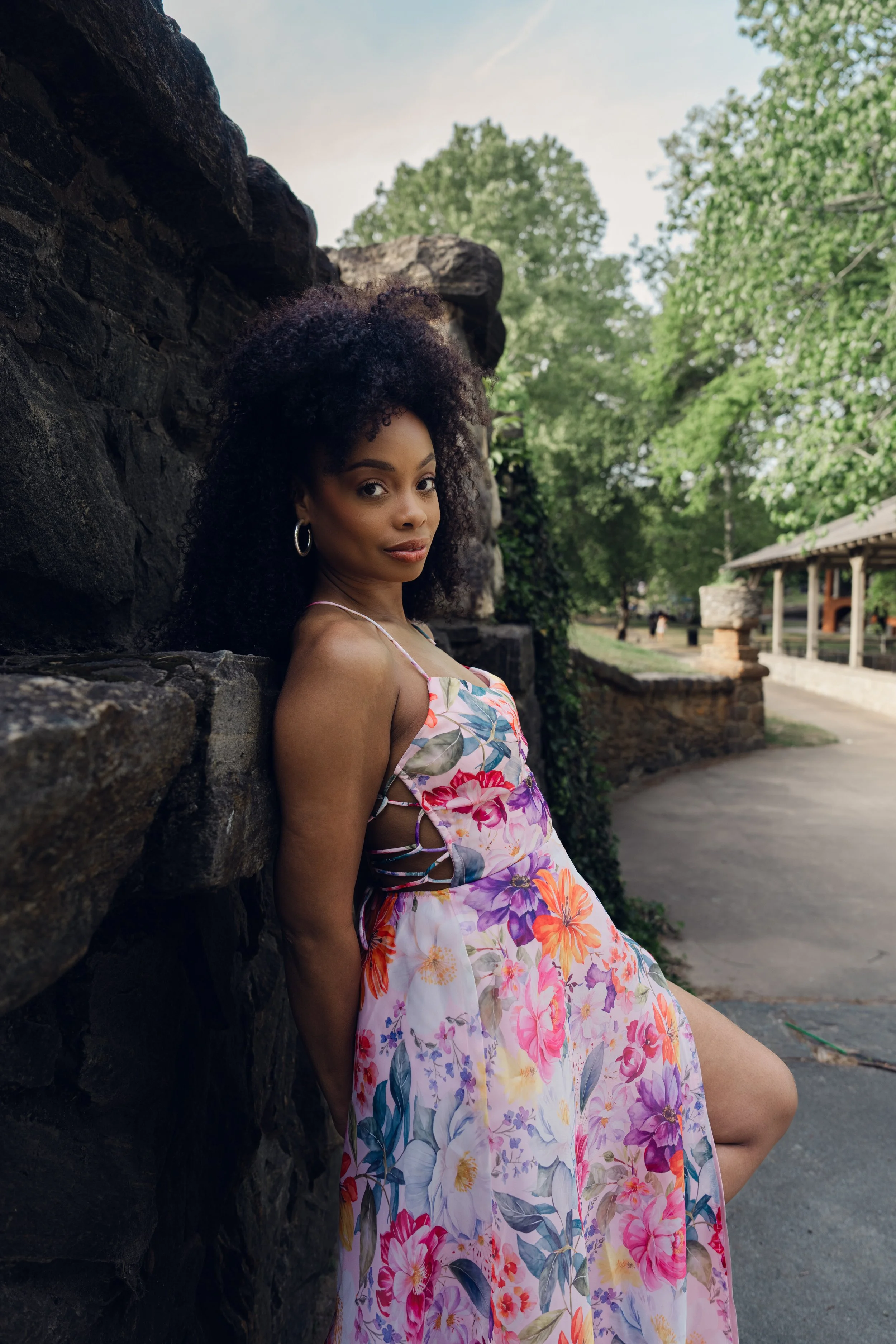 Woman in floral dress leans again stone wall leisurely