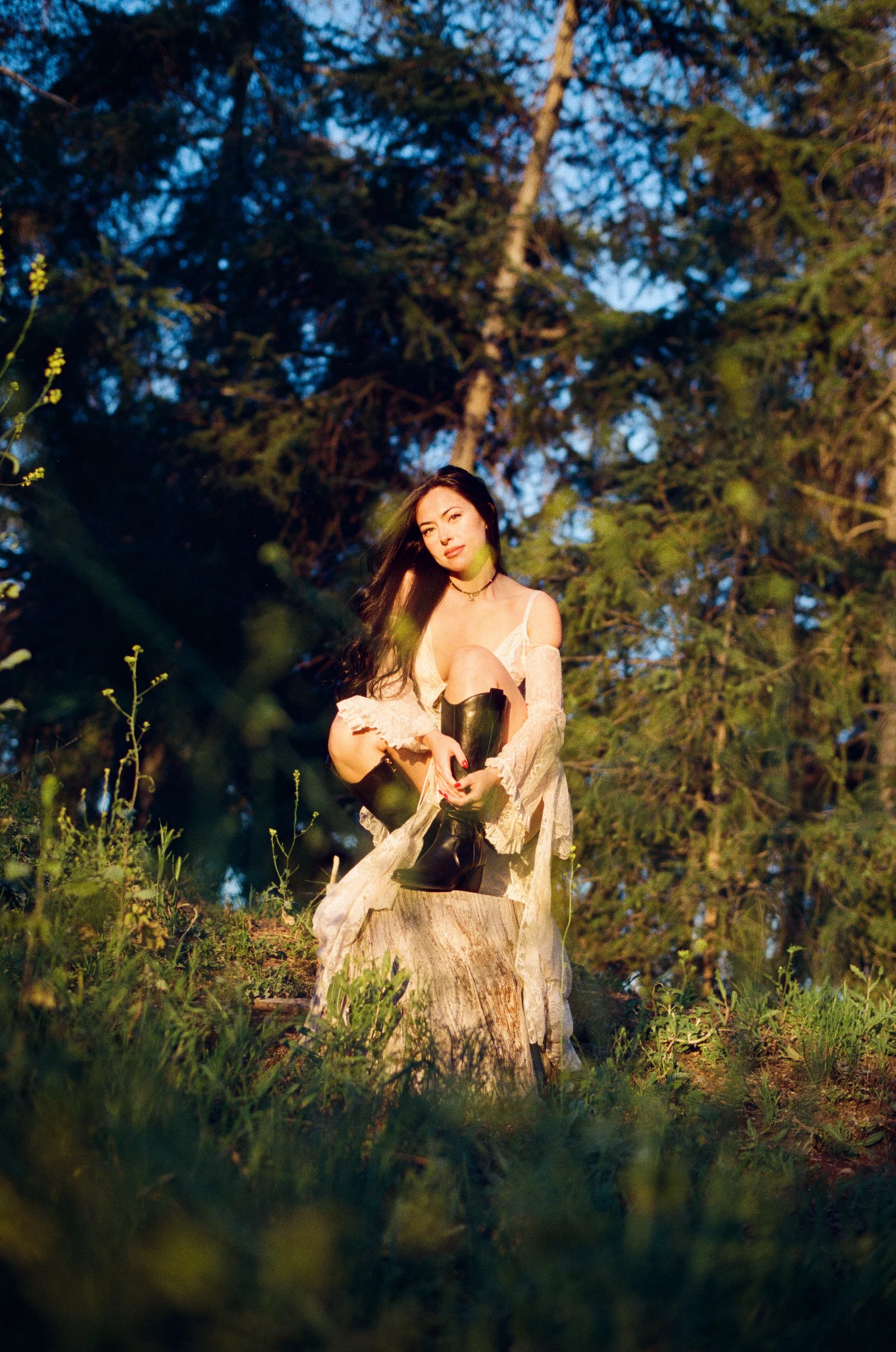 girl in nature wearing white dress and black boots bathed in sunlight
