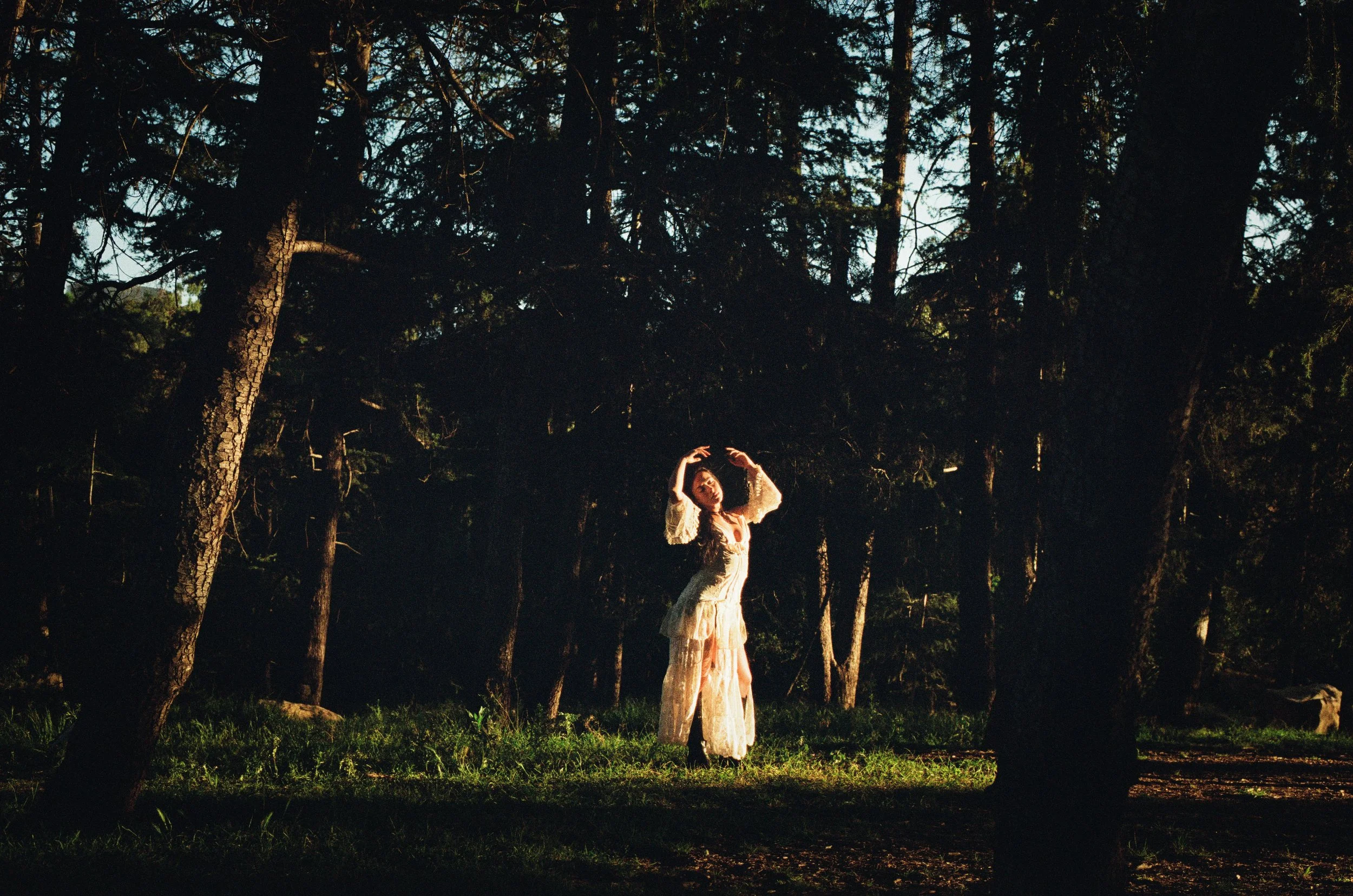 girl in nature wearing white dress and black boots bathed in sunlight