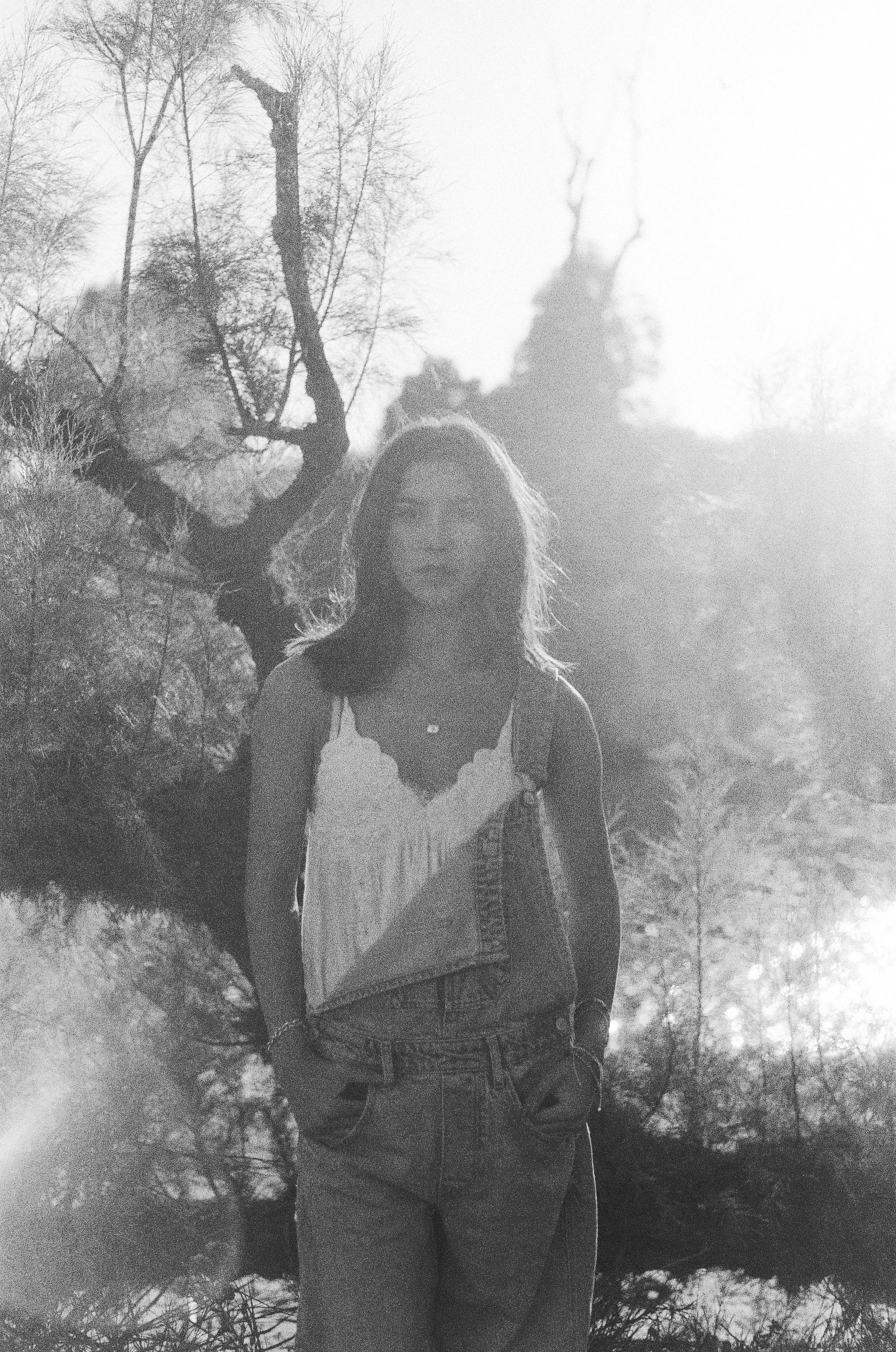 girl in black and white stand among trees in overalls