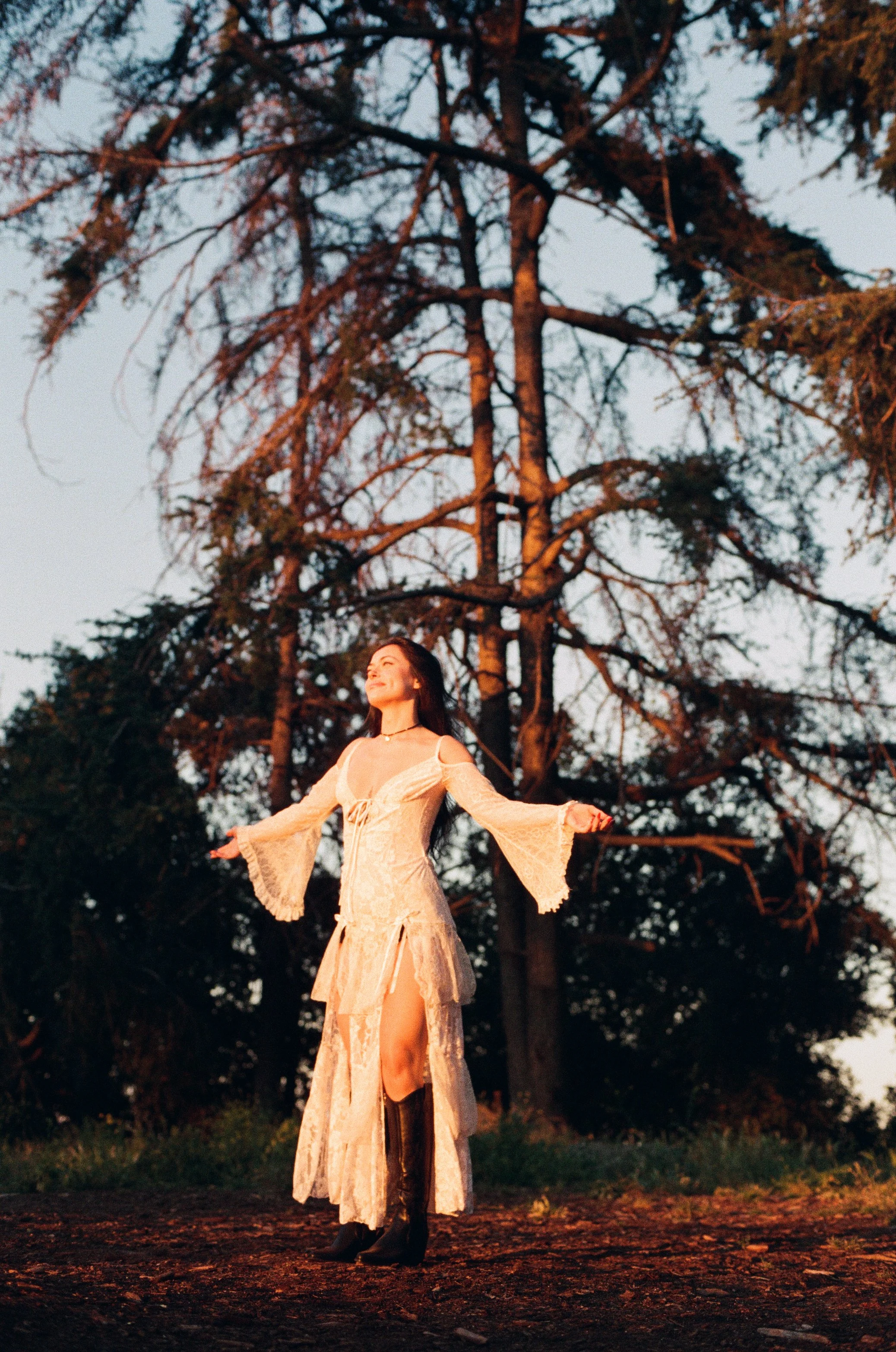 girl in nature wearing white dress and black boots bathed in sunlight