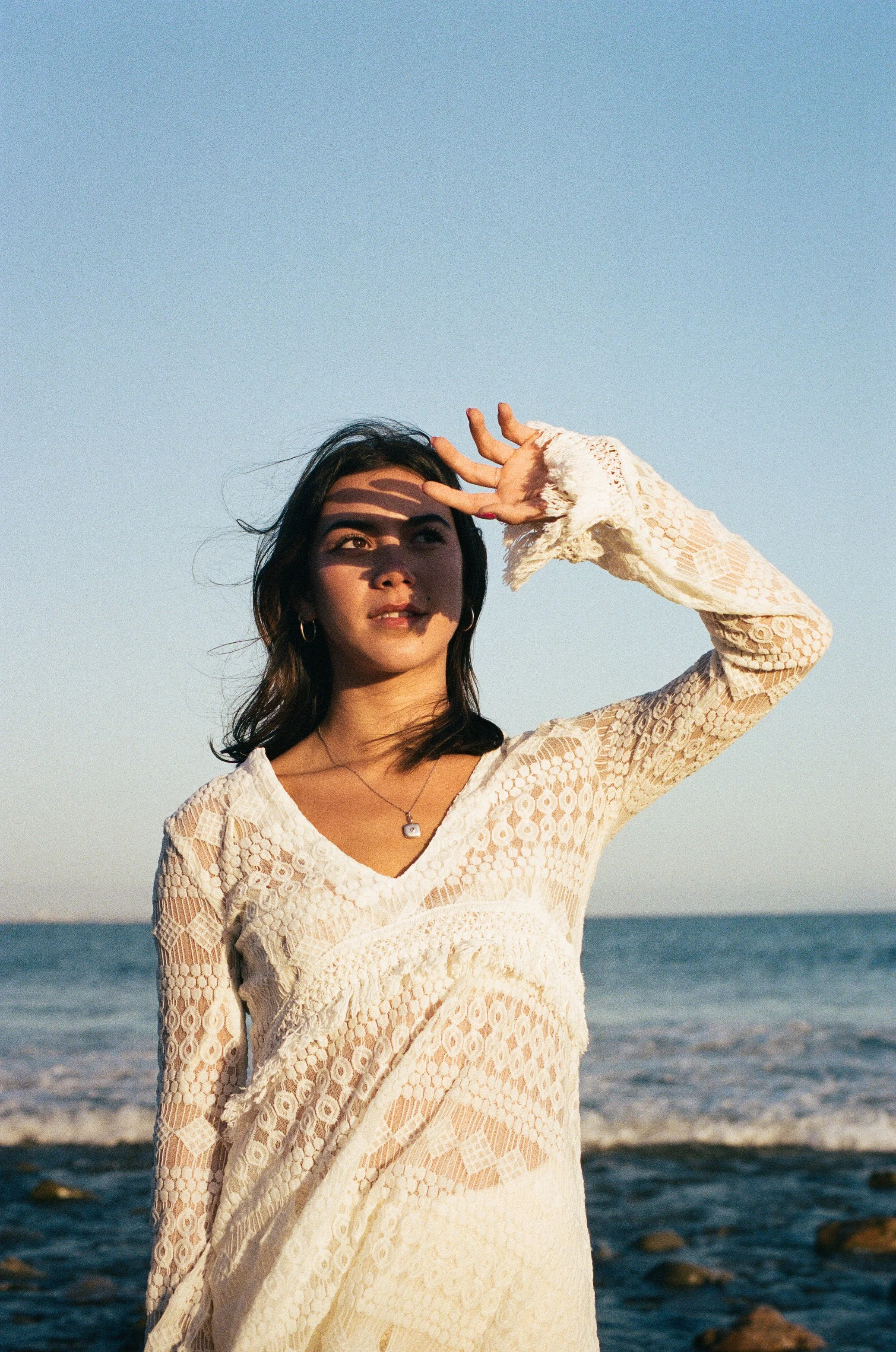 girl stands on beach with her face shadowed from the sun
