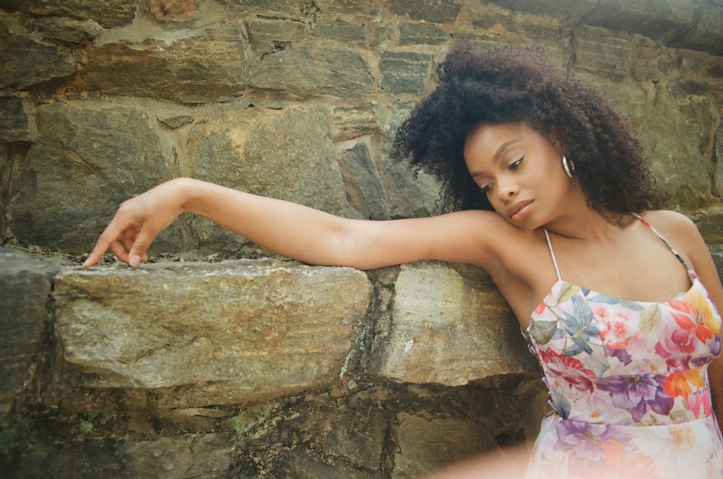 Woman in floral dress leans against stone wall
