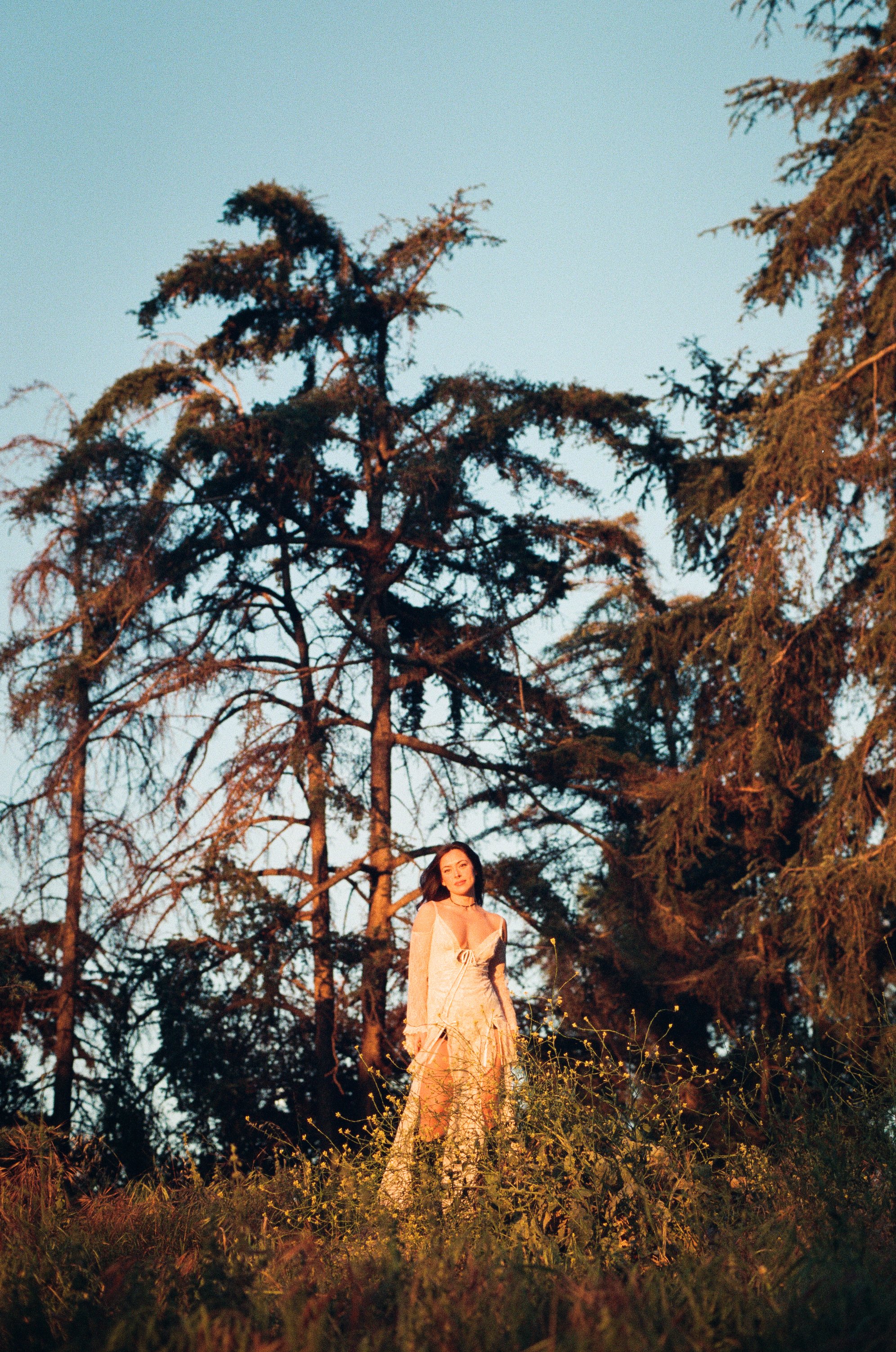 girl in nature wearing white dress and black boots bathed in sunlight