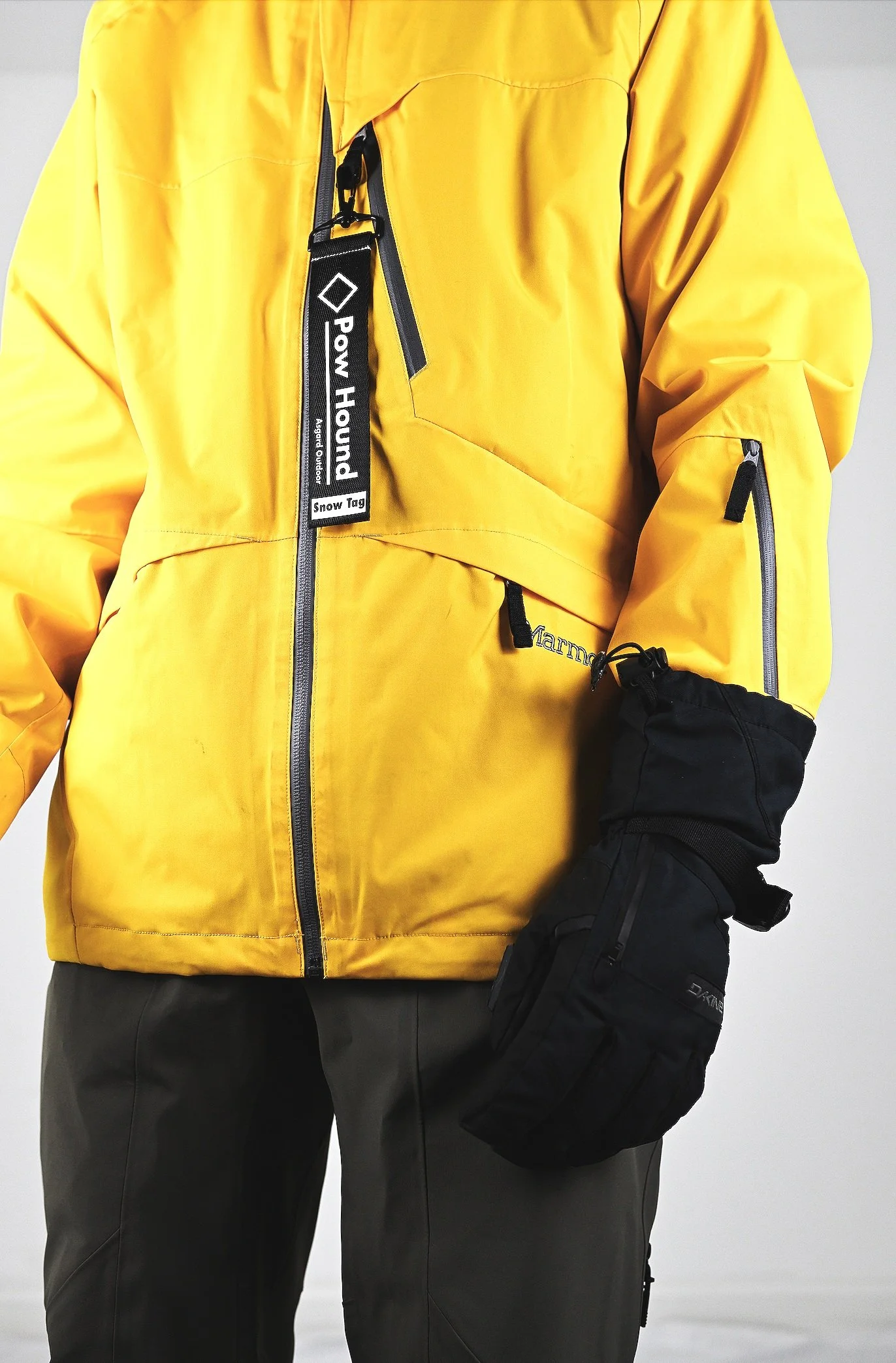 Close-up of a person wearing a bright yellow Marmot ski jacket with black gloves and gray pants, showcasing outdoor winter gear.