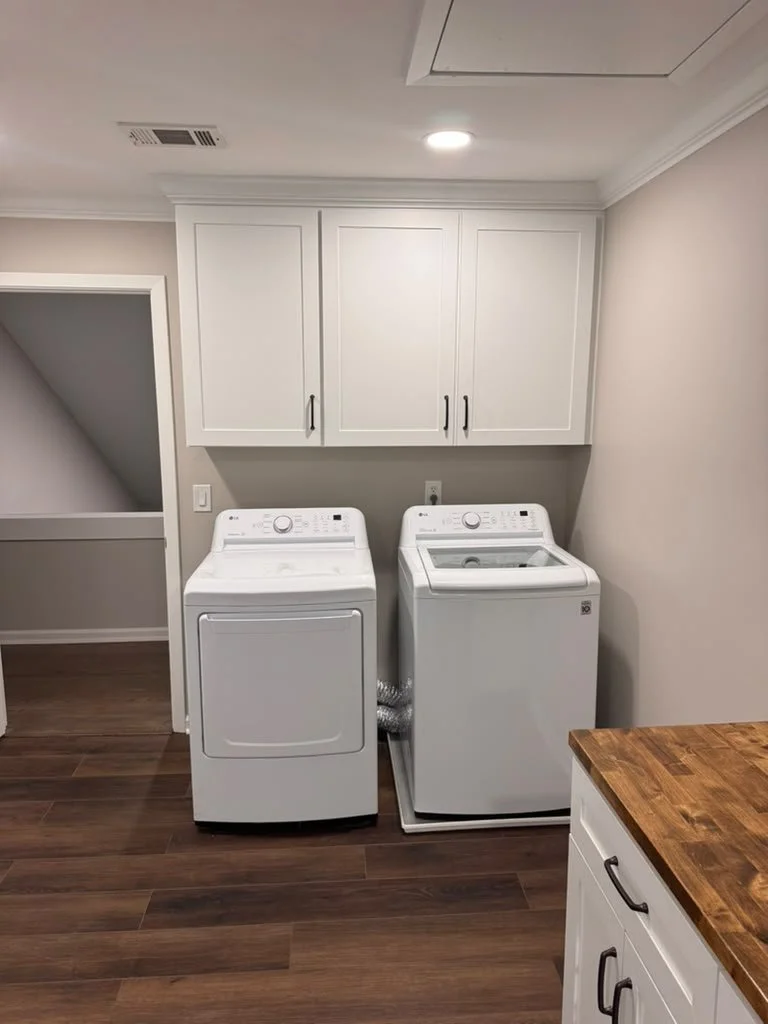 Washer and dryer with custom white shaker upper cabinets in a remodeled laundry room