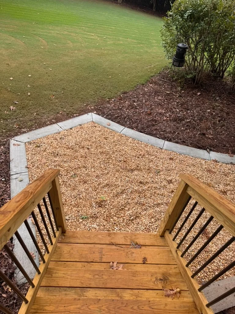 New pressure-treated deck stairs with black metal balusters leading to a pea gravel landing in East Cobb, GA
