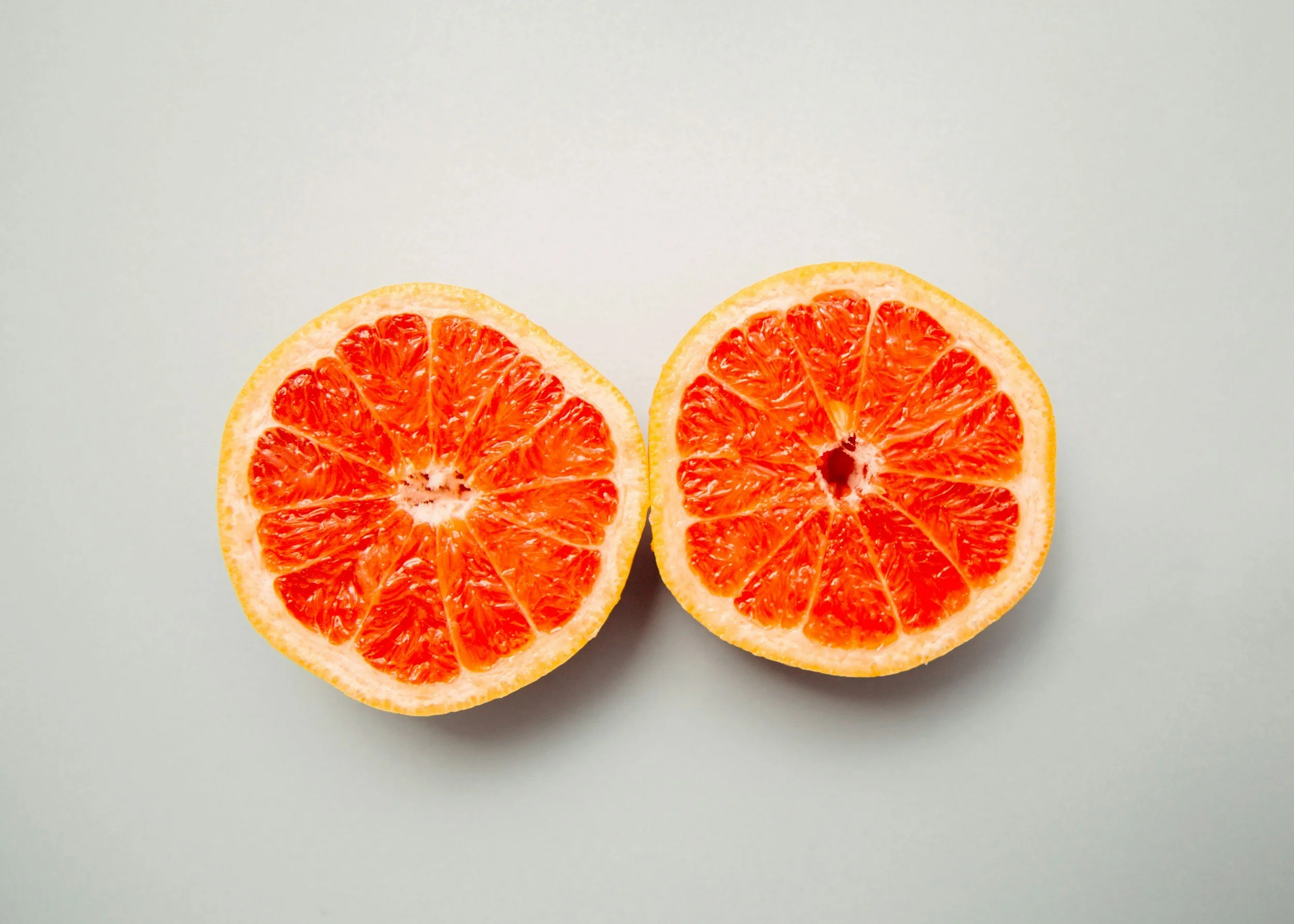 Two halves of a grapefruit placed on a light-colored surface.