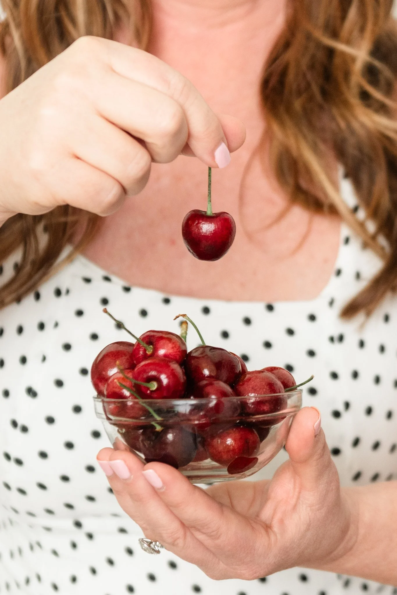 Person holding a bowl of cherries and about to pick a cherry