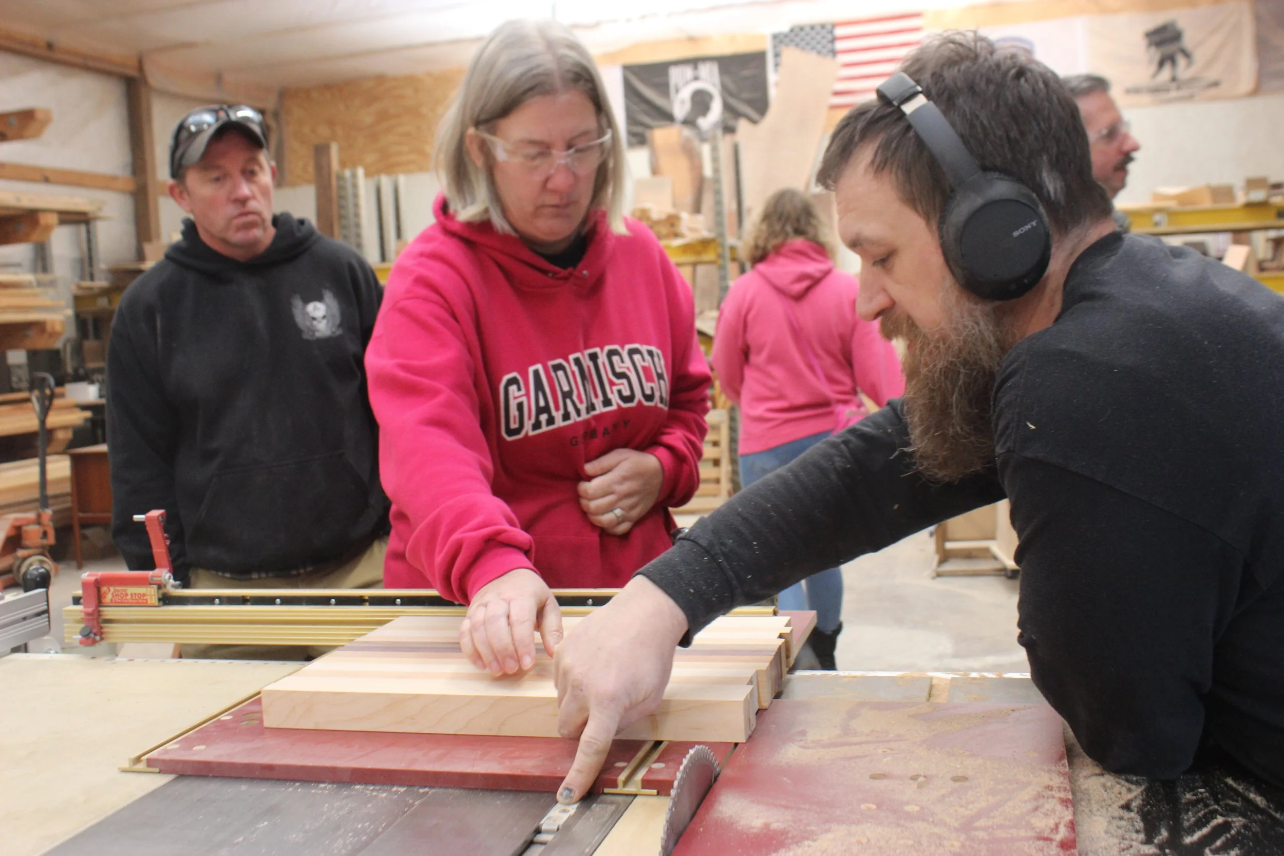 Owner Kurt Ballash teaching a woman in a pink sweater  on how to use a piece of equipment in the workshop.