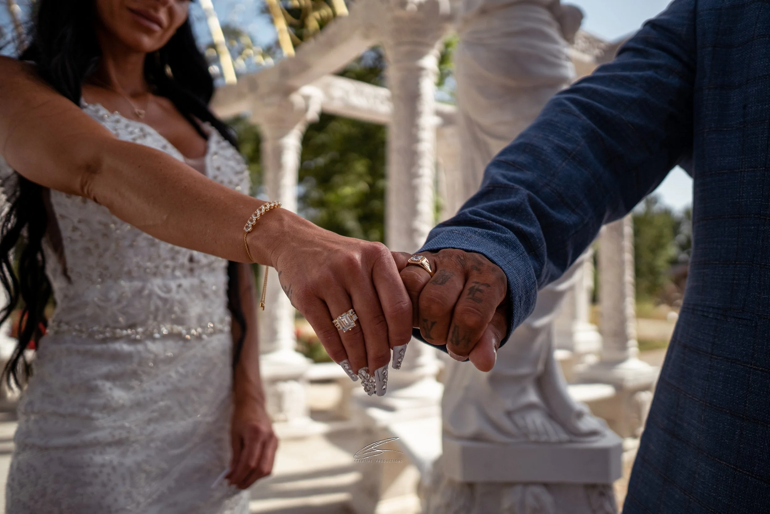Nahaufnahme eines Heiratszeremonie mit vereinten Händen eines Paares, Frauenring mit Diamant, Frauenarmband, männlicher Ring, beide Paare mit tätowierten Händen, im Freien bei Sonnenschein.