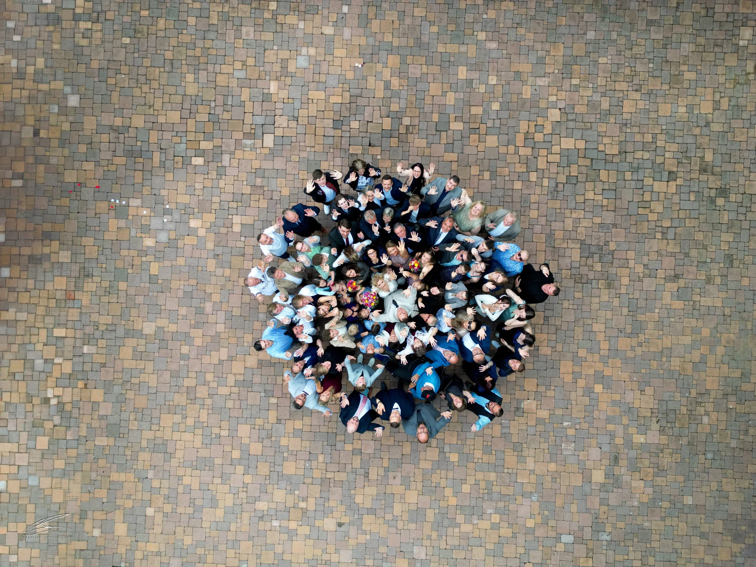 Vogelperspektive auf eine Gruppe von Menschen, die in einem Kreis auf einer gepflasterten Fläche stehen und nach oben schauen.