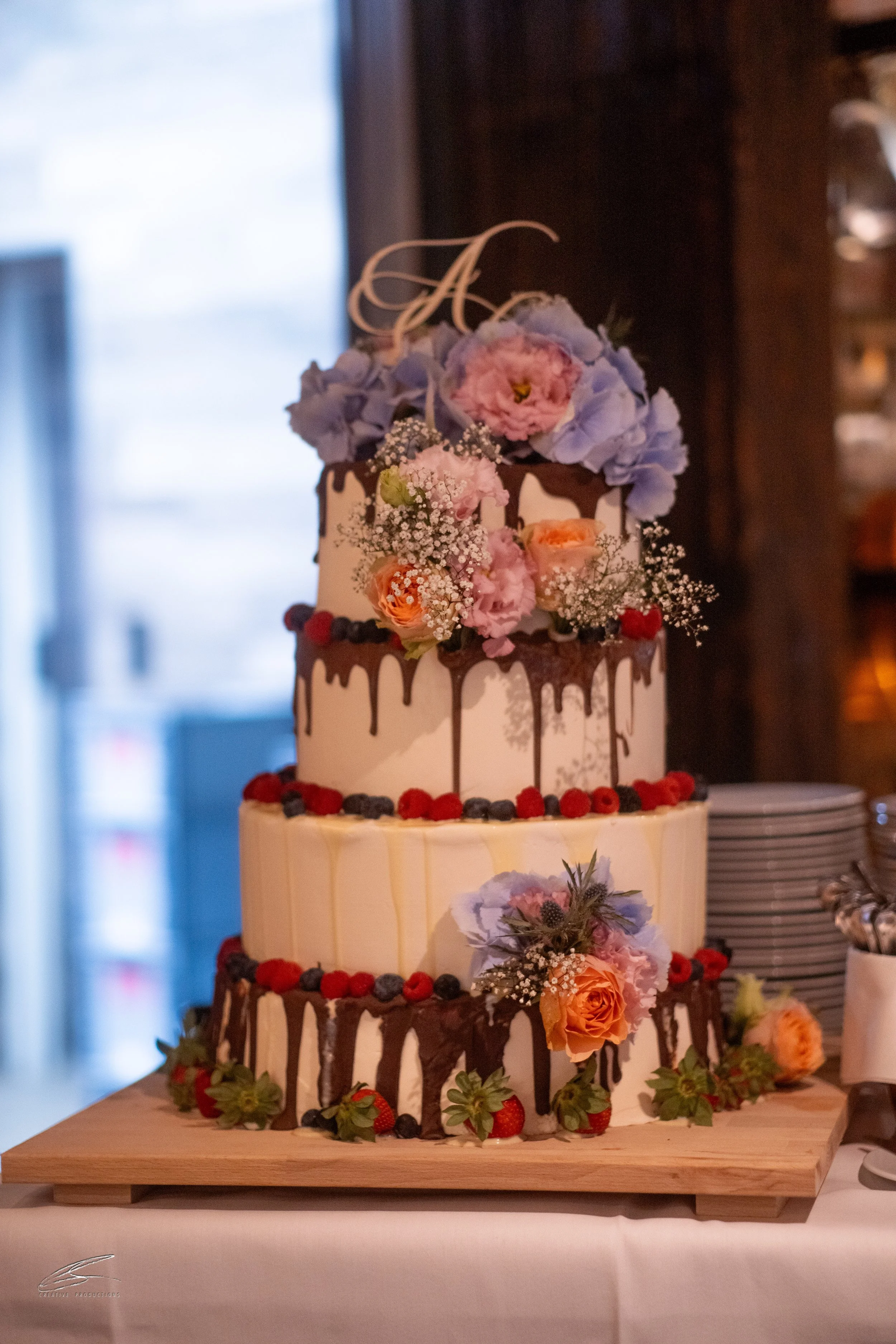 Dreistöckige Hochzeitstorte mit Blumen und Beeren, dekoriert mit Schokolade und bunten Früchten.