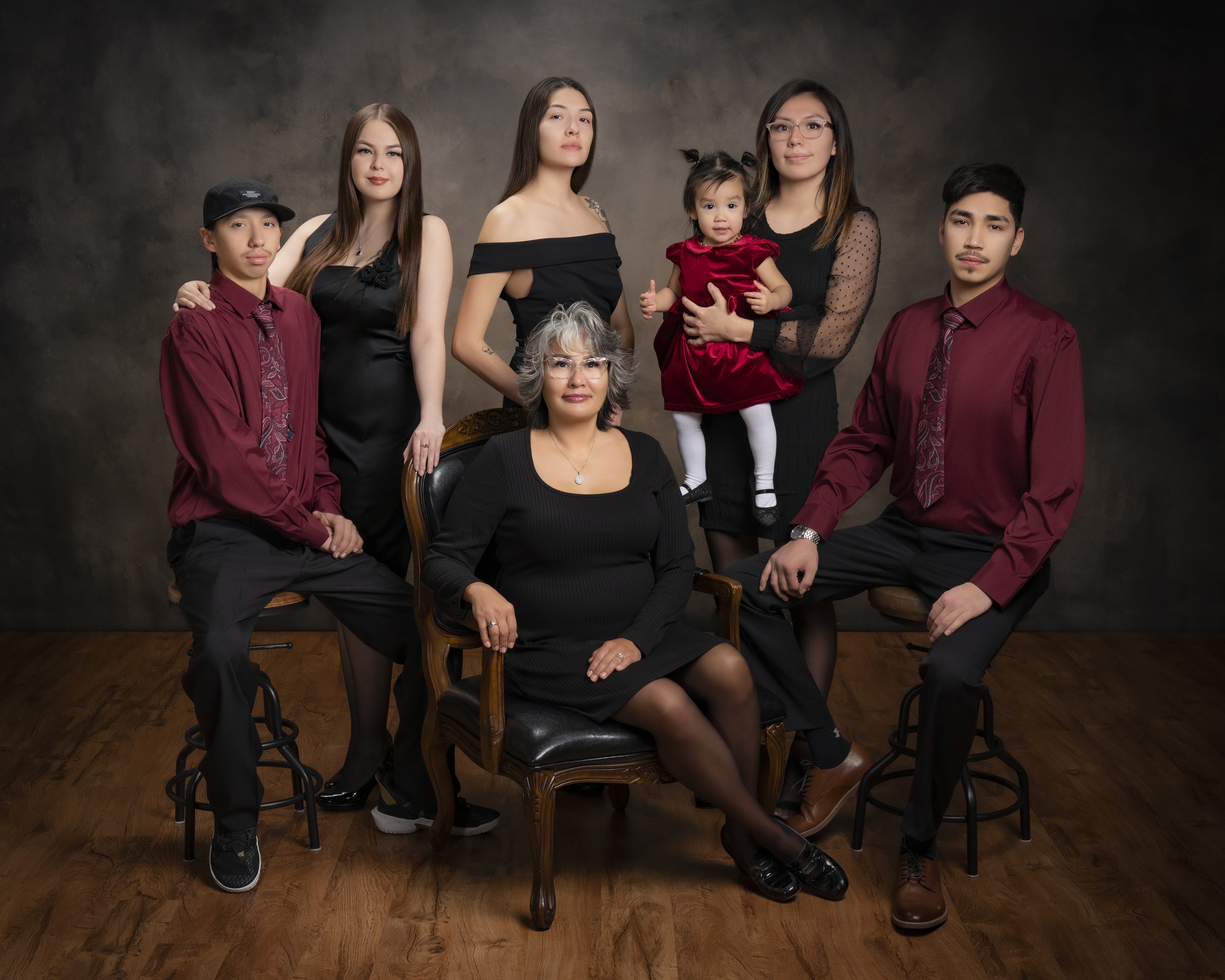 Family portrait with seven people, including a seated older woman, standing young adults in formal attire, and a child in a red dress.