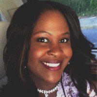 A woman with dark hair smiling inside a car