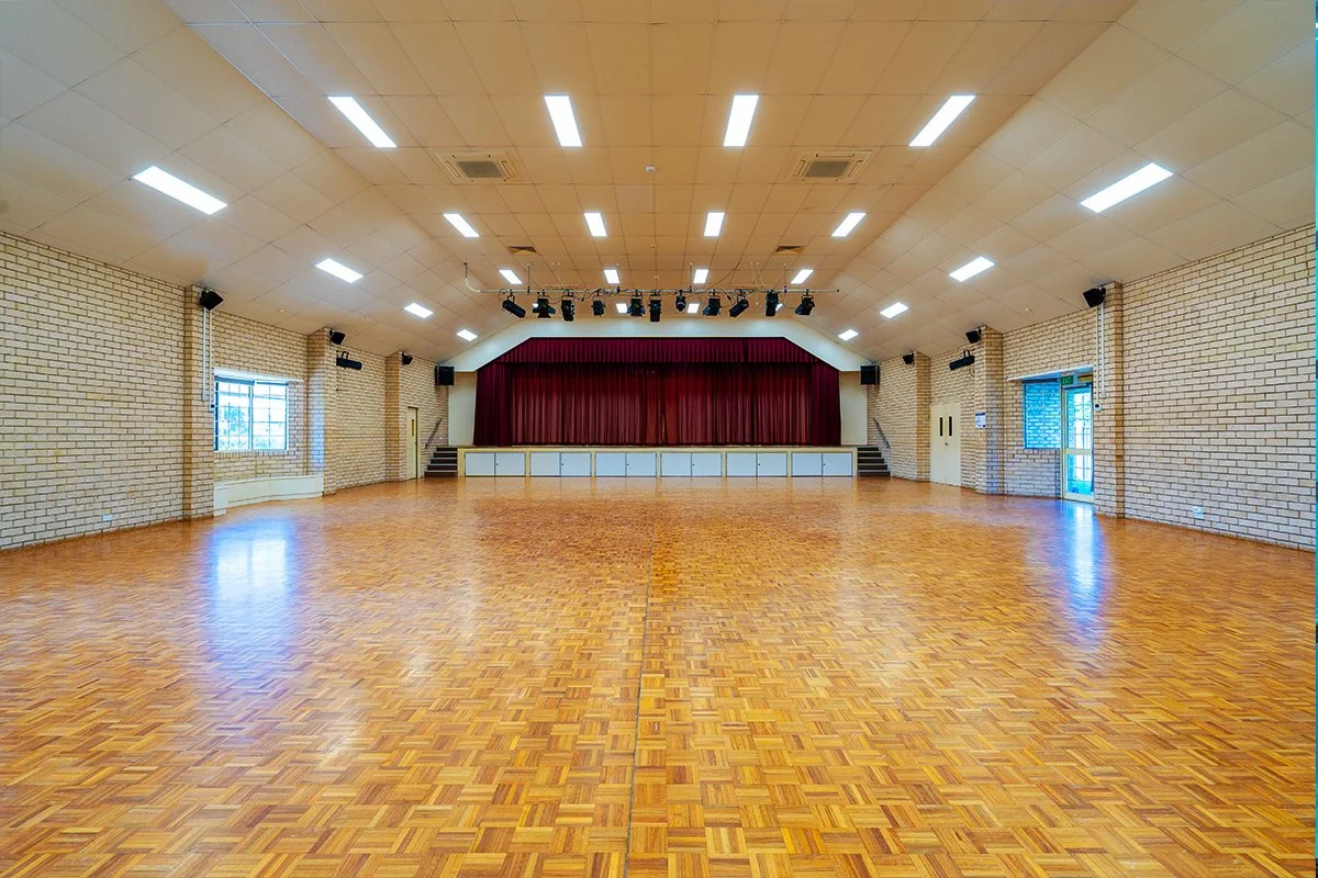 Empty indoor stage with red curtains, wooden floor, and brick walls, decorated for events or performances.