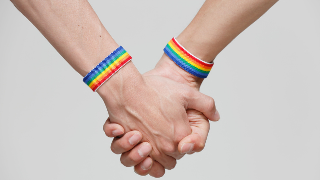 two hands holding each other and wearing rainbow bracelets to represent lgbtq affirming therapy intensive