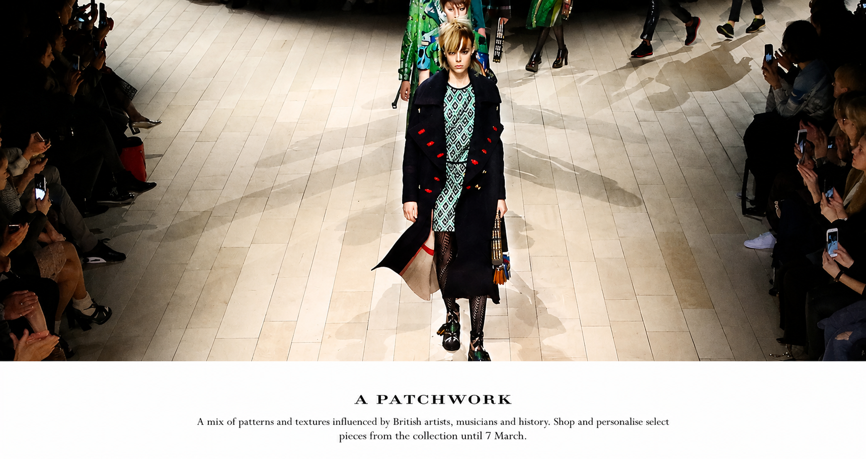 Fashion models walk down a runway during a fashion show, with audience members seated on either side taking photos.