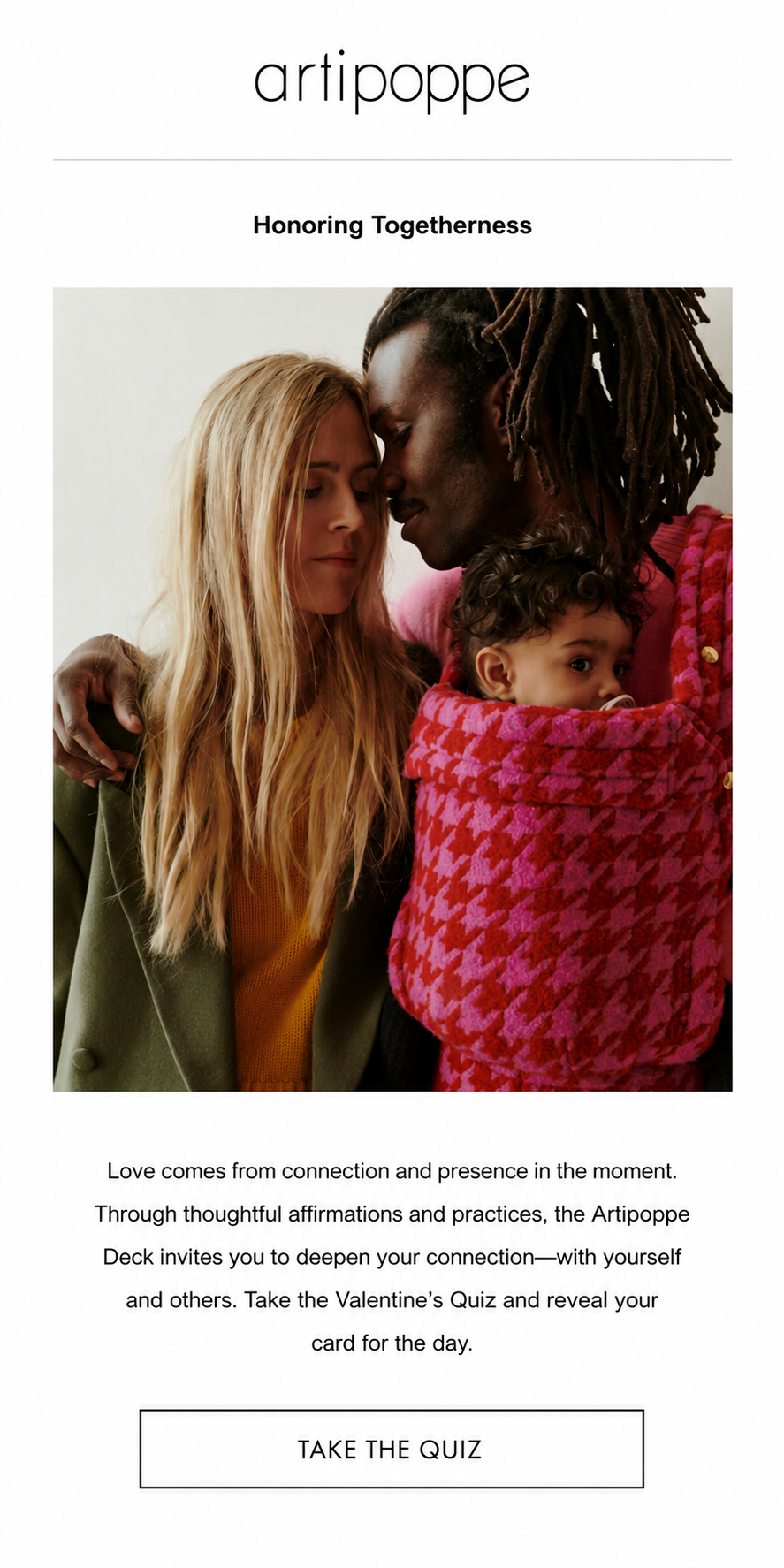A close-up of two people wearing colorful sweaters with one in an olive green coat over a mustard yellow top and the other in a pink and red houndstooth pattern sweater. The man is carrying a wearing a baby on his front using an Artipoppe baby carrie