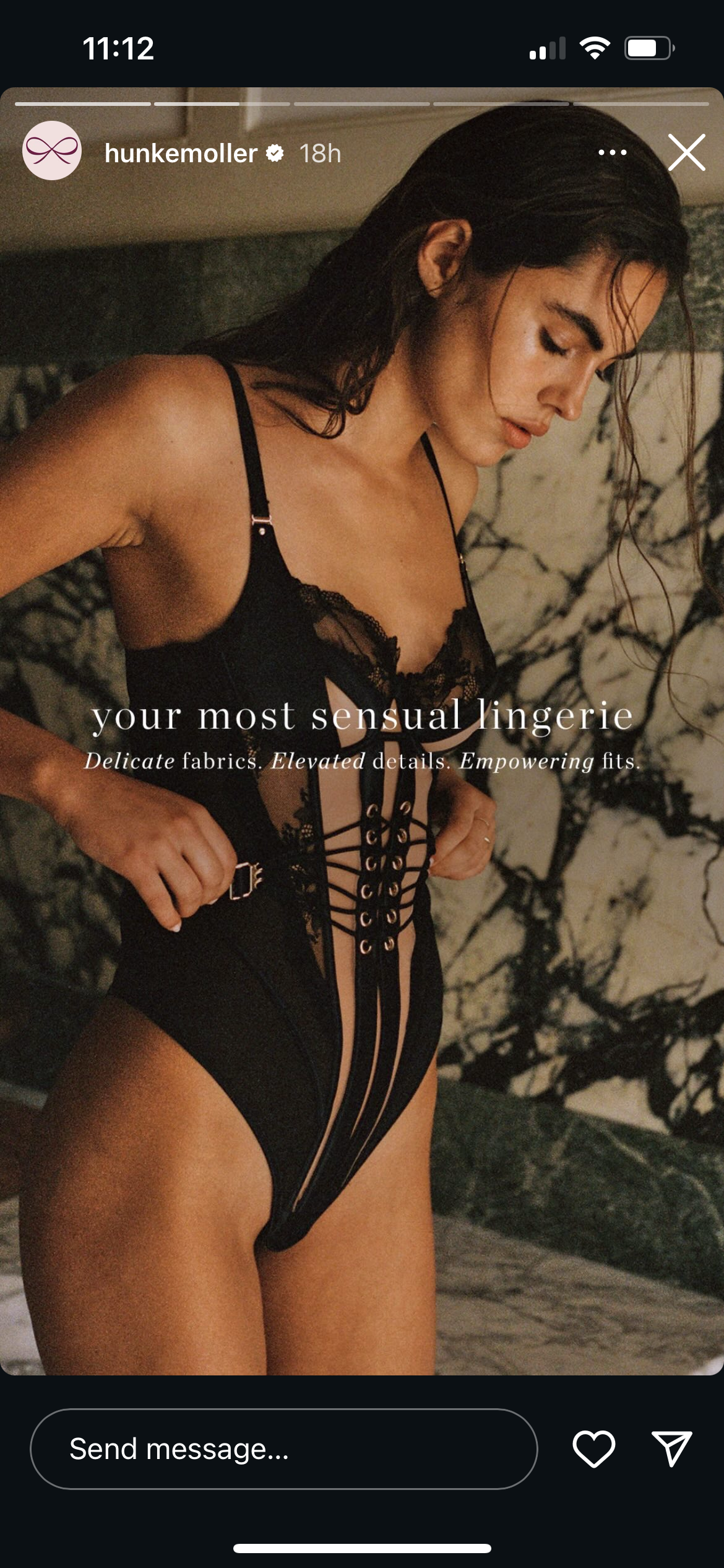 Woman in black lace lingerie with laced-up design, standing indoors against a marble wall.