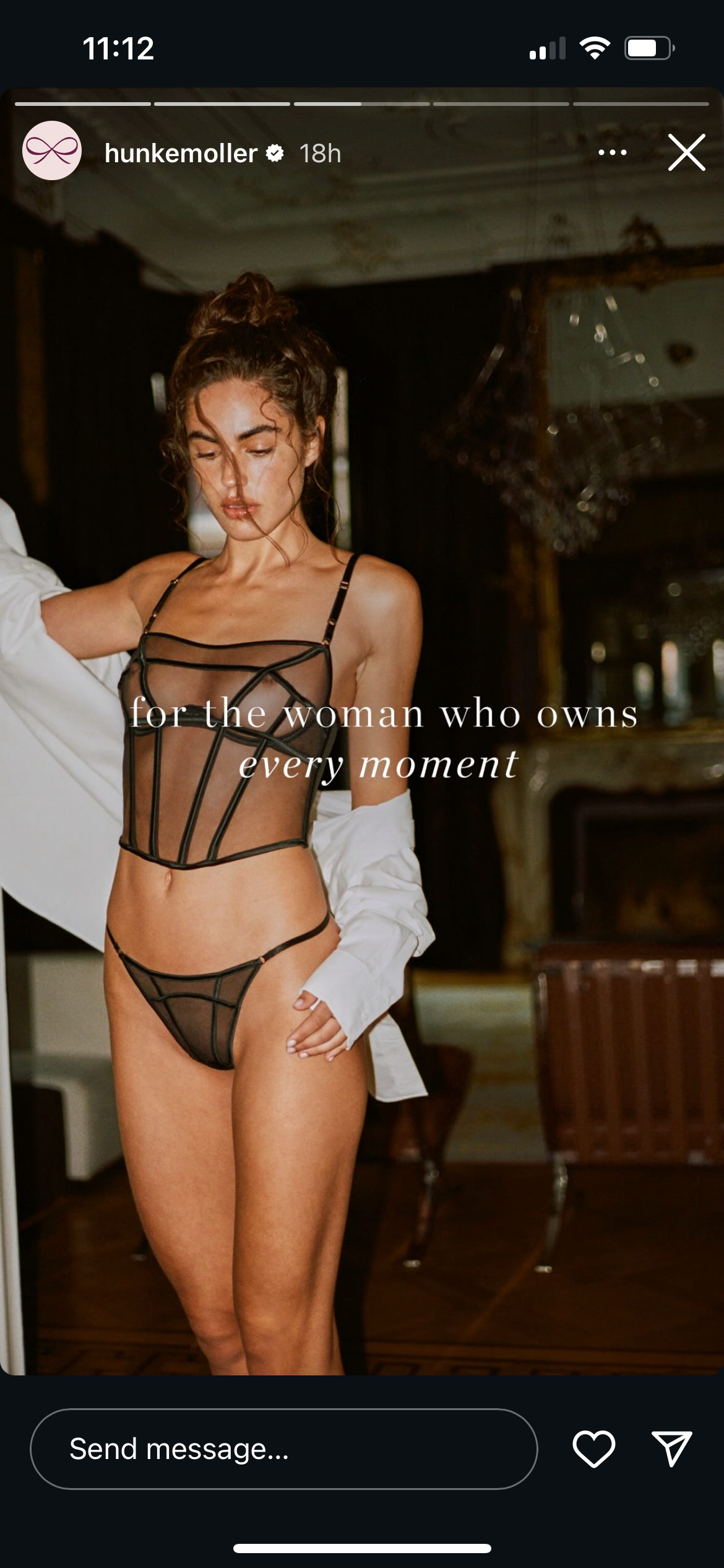 A woman wearing black sheer lingerie with geometric patterns, standing indoors in front of a mirror and elegant furniture, with the text 'for the woman who owns every moment' overlayed.