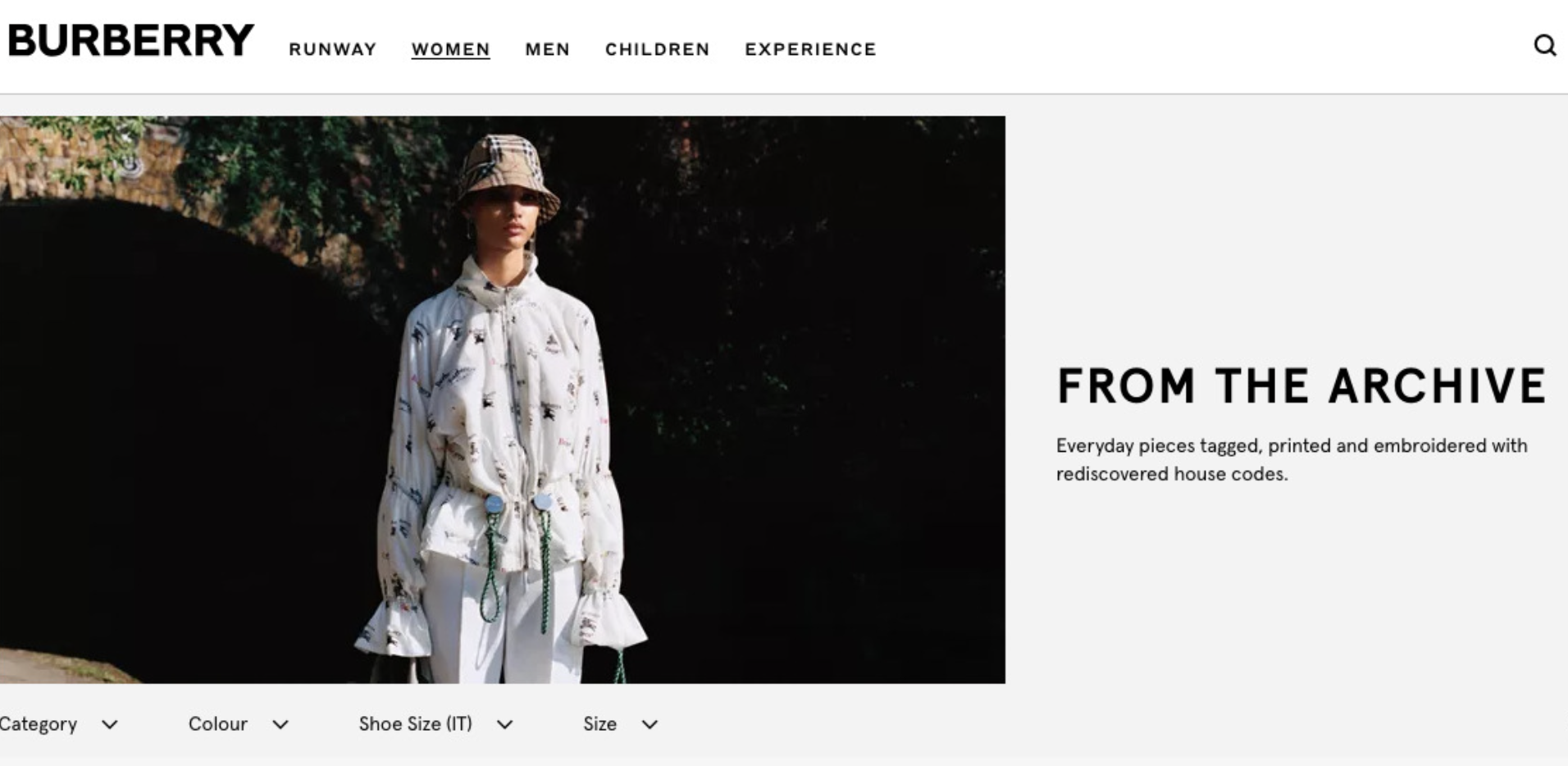 Model wearing a printed Burberry jacket, white pants, and a Burberry bucket hat, standing outdoors against a dark background.