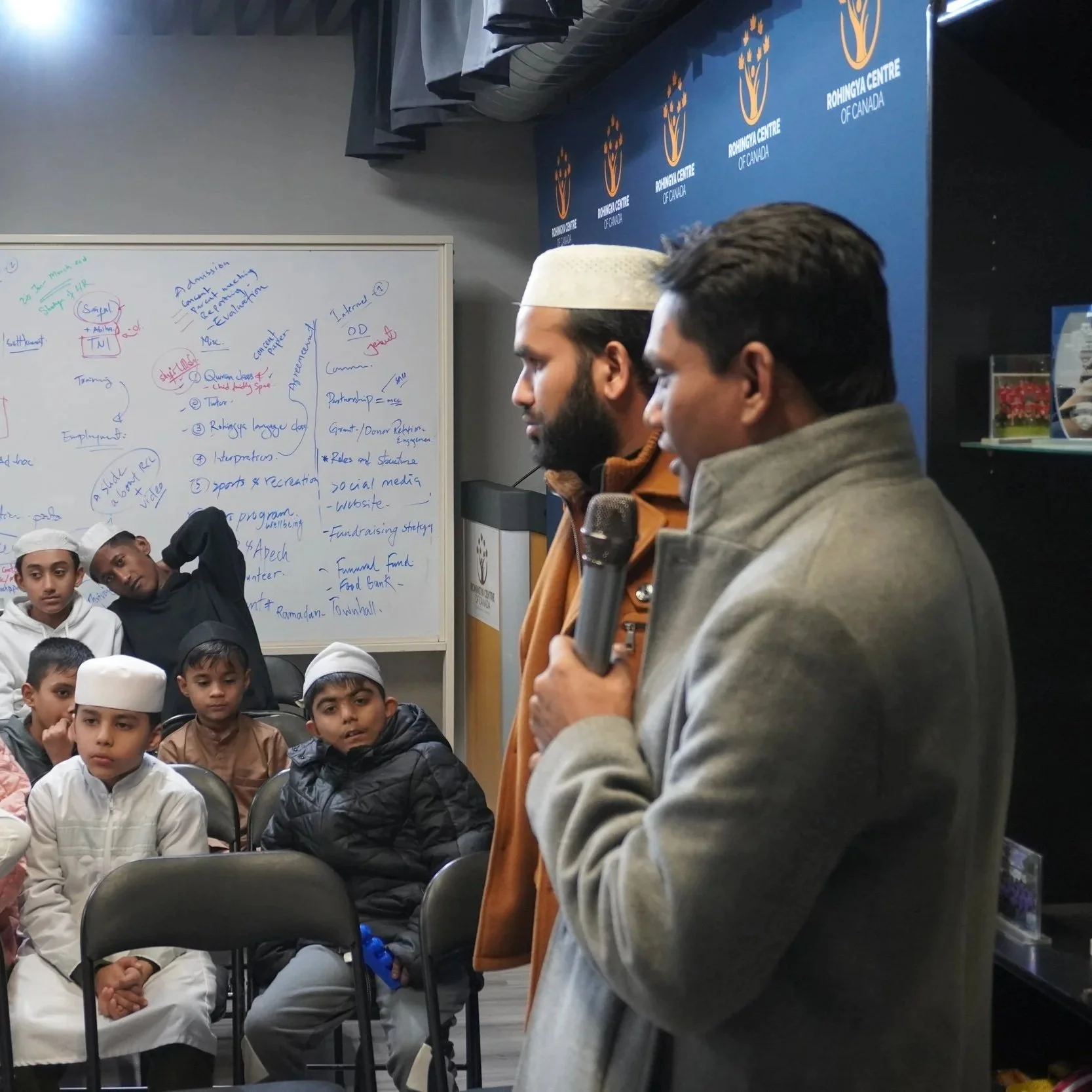 Many children sitting in a classroom listening to the teachers as they take Rohingya language lessons