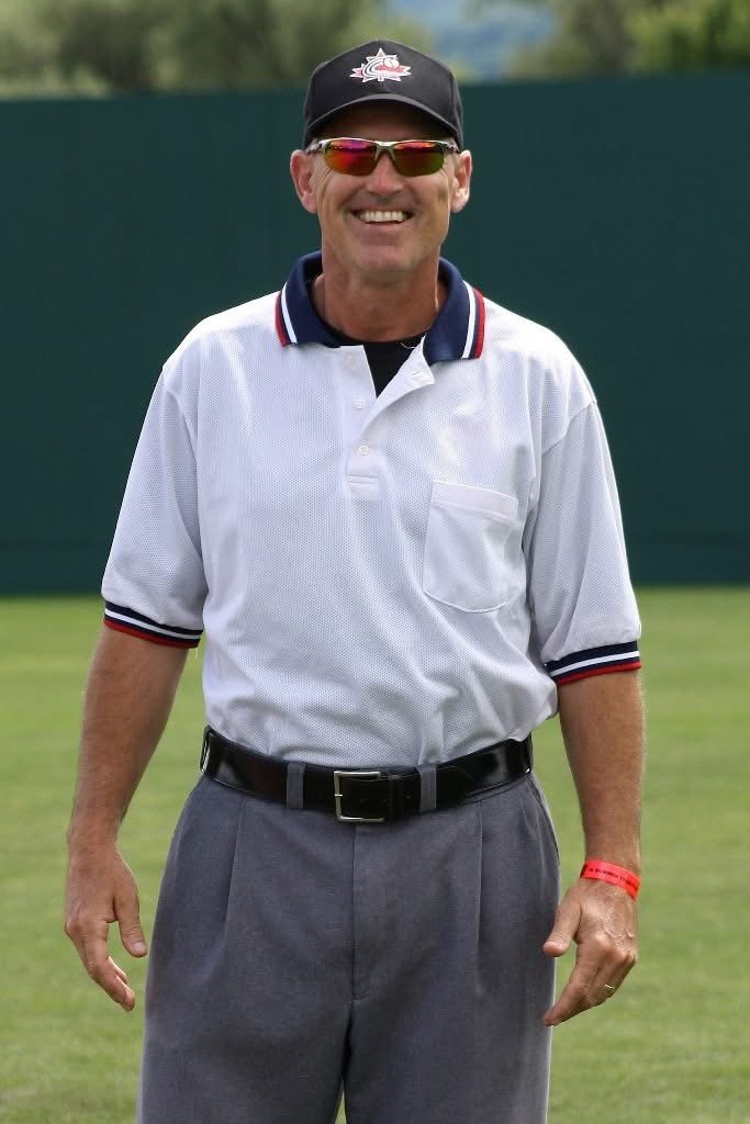 Dean smiling outside wearing hat, sunglasses, and in a baseball umpire uniform