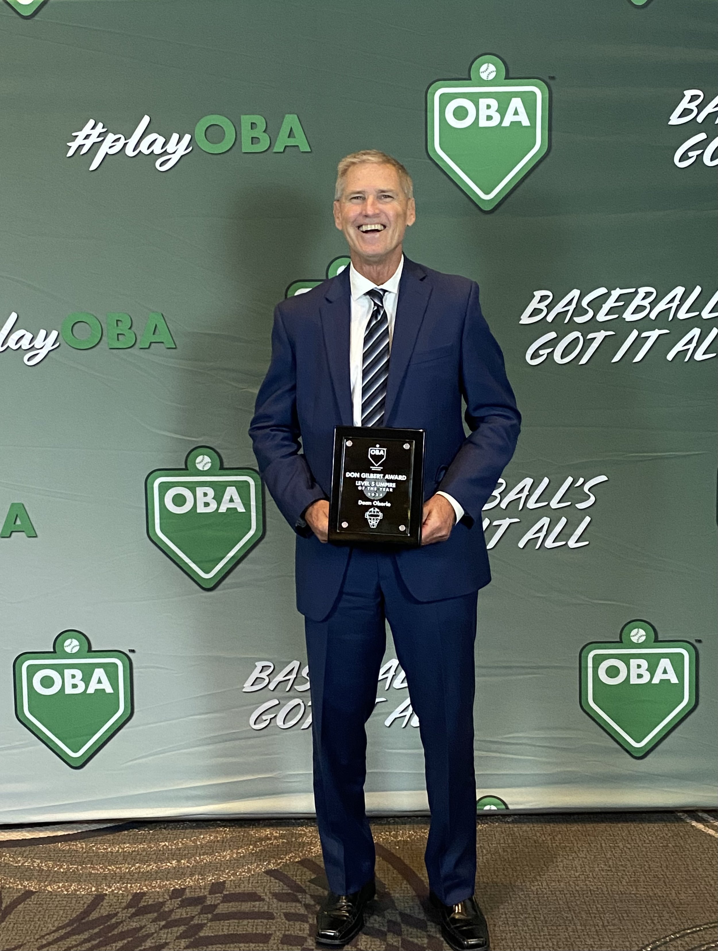Dean holding plaque award in front of OBA banner