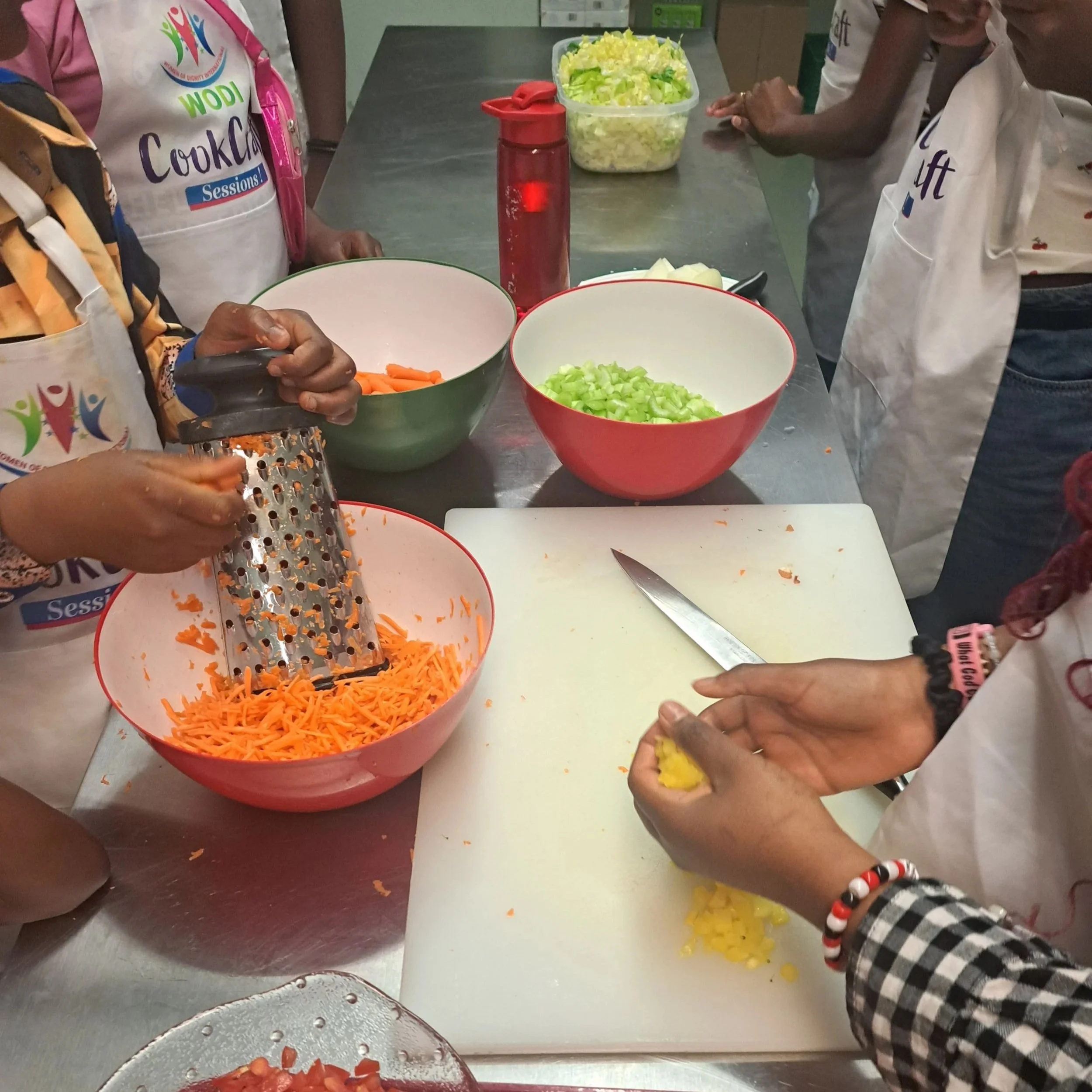 Hands grating carrots and chopping various vegetables to go into colourful bowls