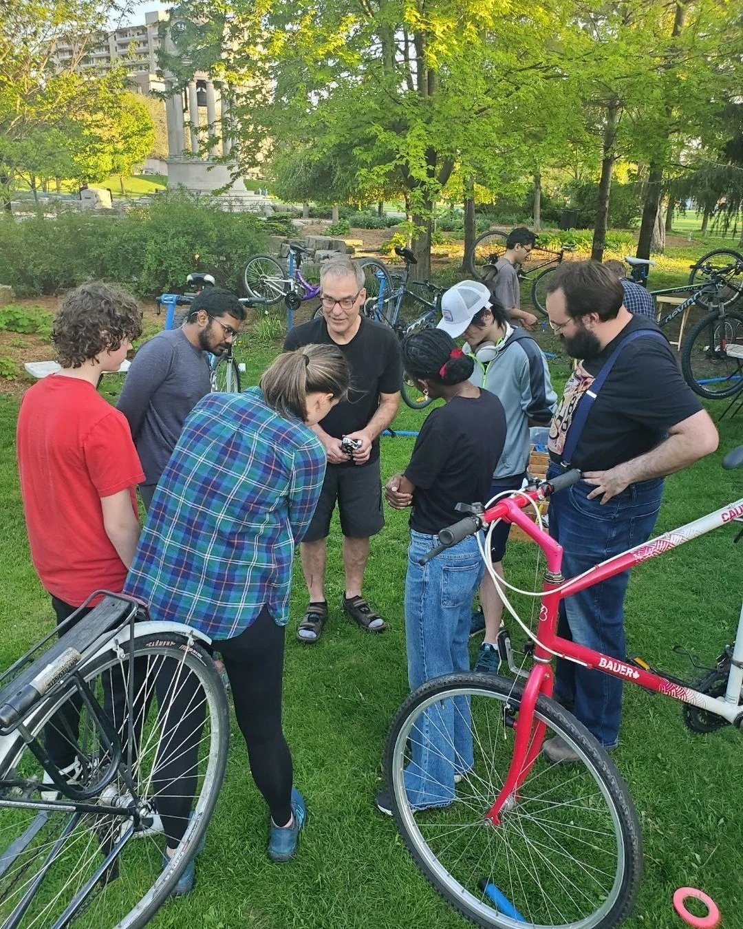 A group of people standing in a circle outside with their bikes listening to the instructor teach them how to ride