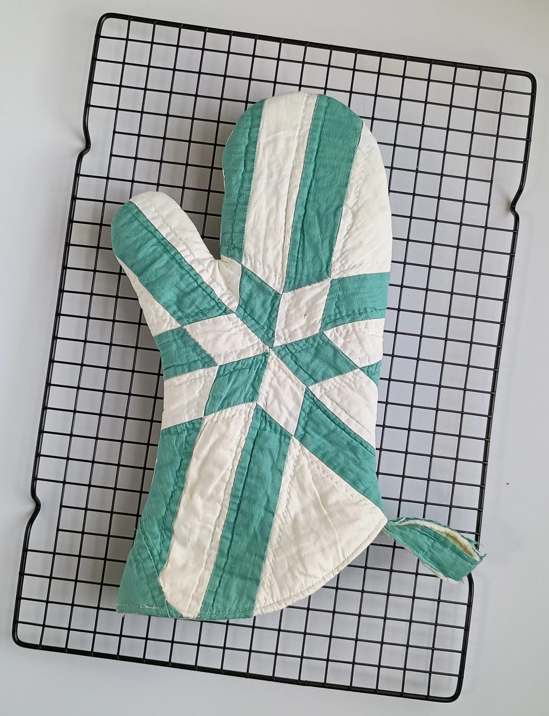 A green and white oven mitt made from an antique quilt with a star pattern
