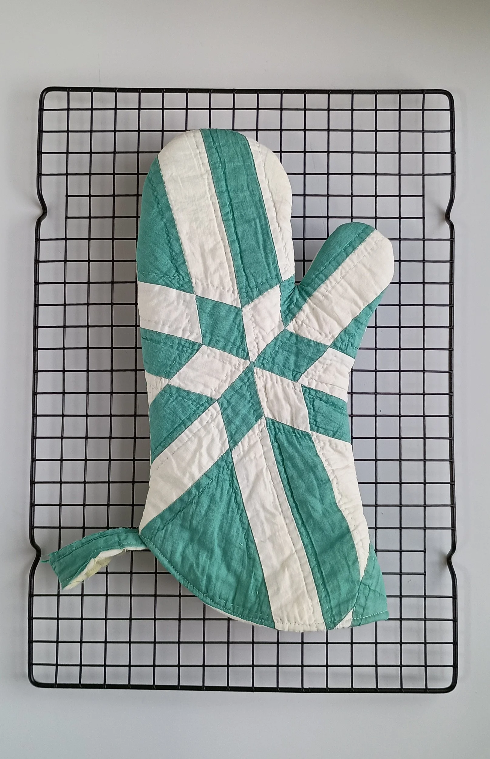A green and white oven mitt made from an antique quilt with a star pattern