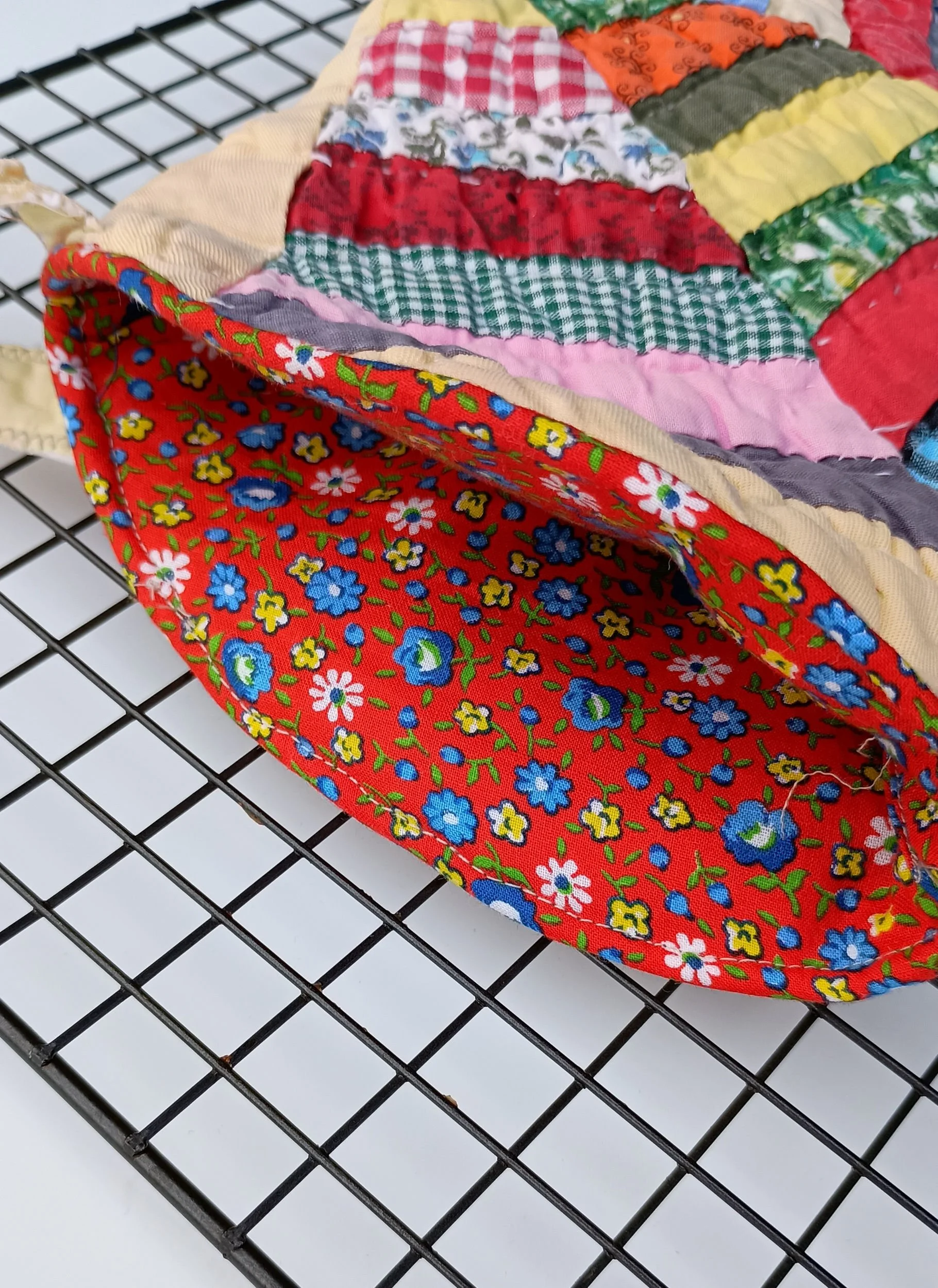 An inside view of an oven mitt made from a brightly colored antique quilt