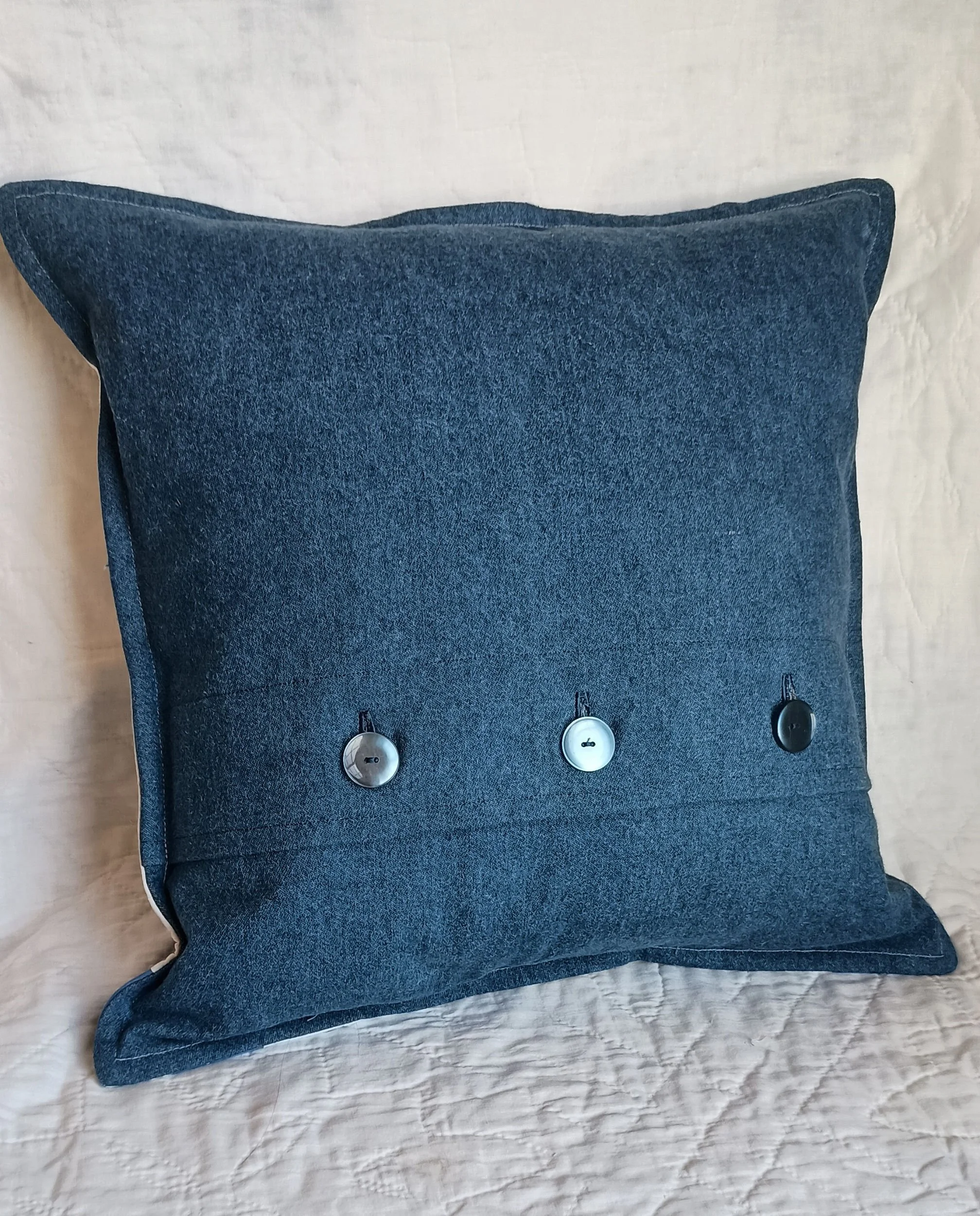 The denim backside of a decorative quilt pillow with a button closure