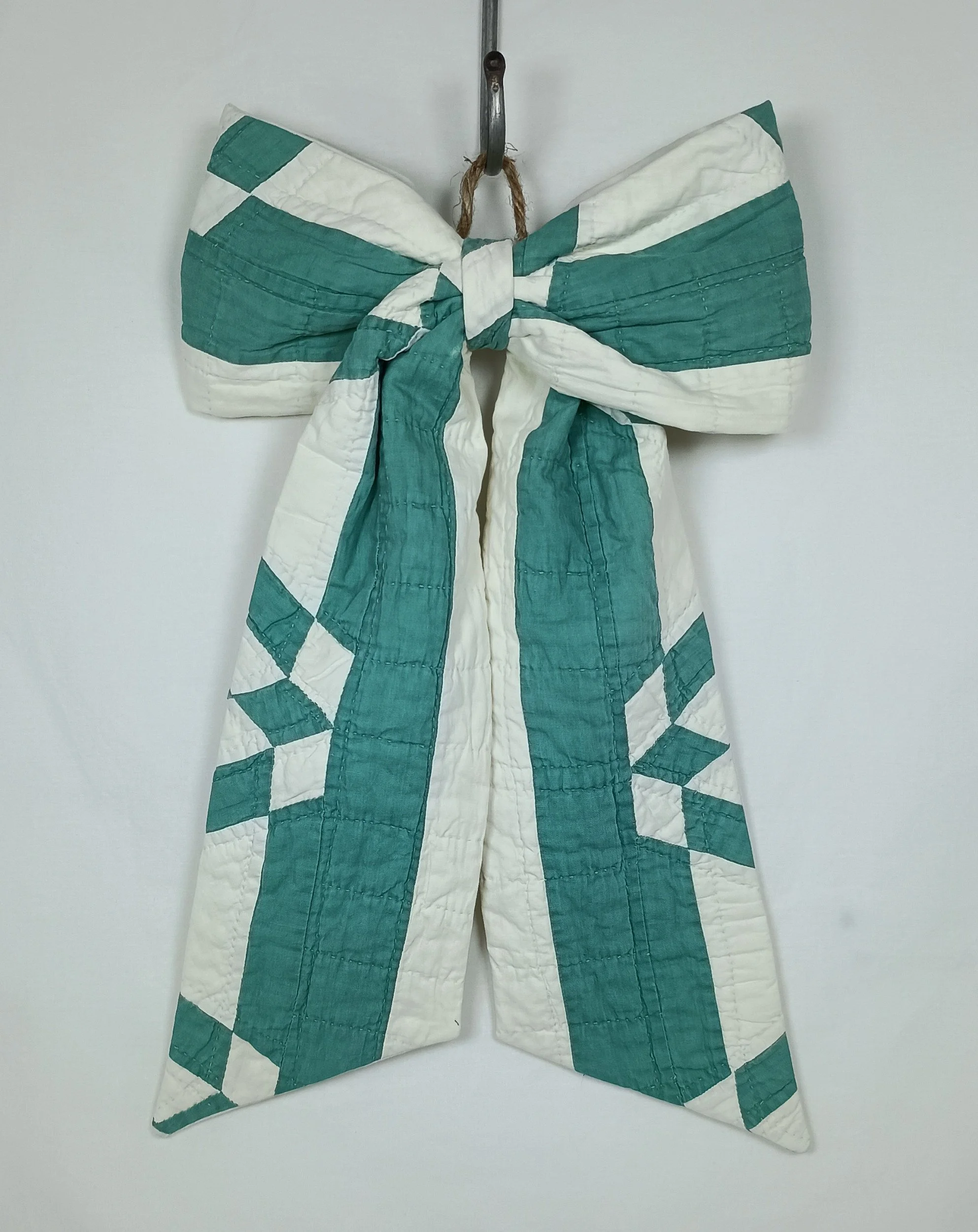 A green and white decorative bow made from an antique quilt