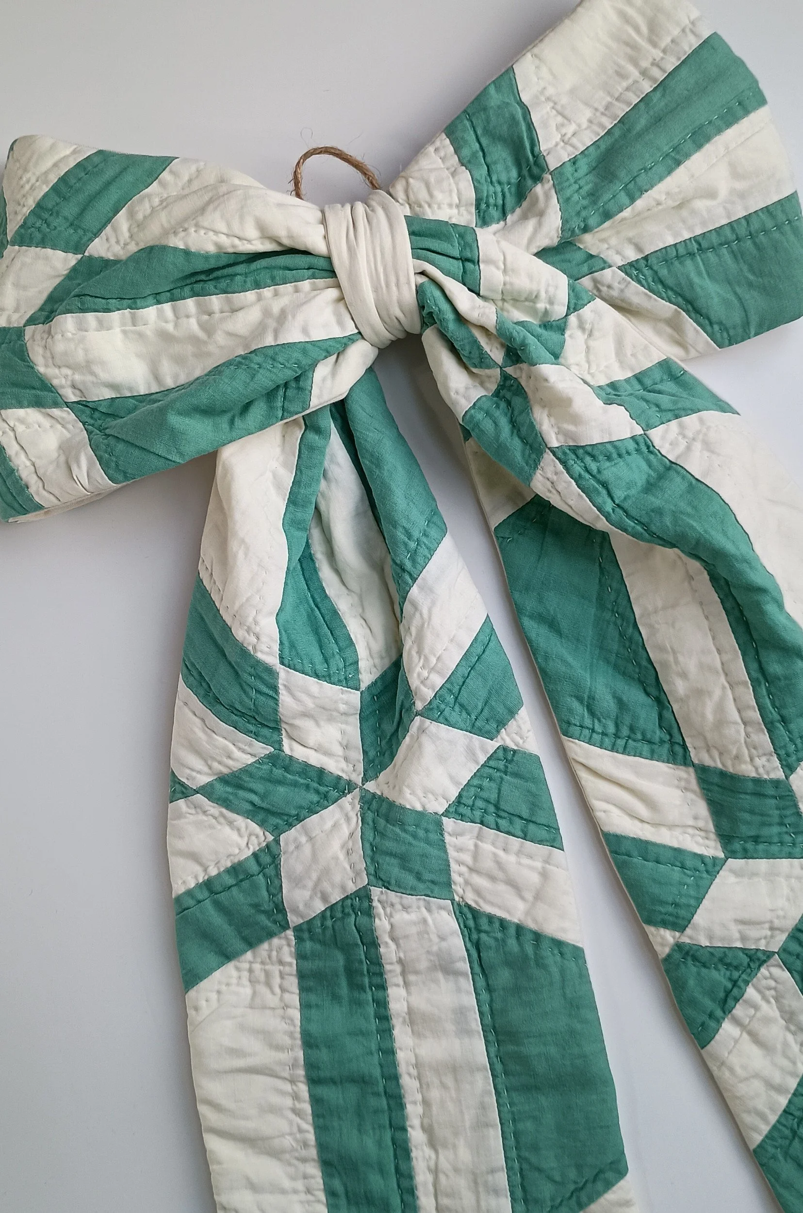 A green and white decorative bow made from an antique quilt