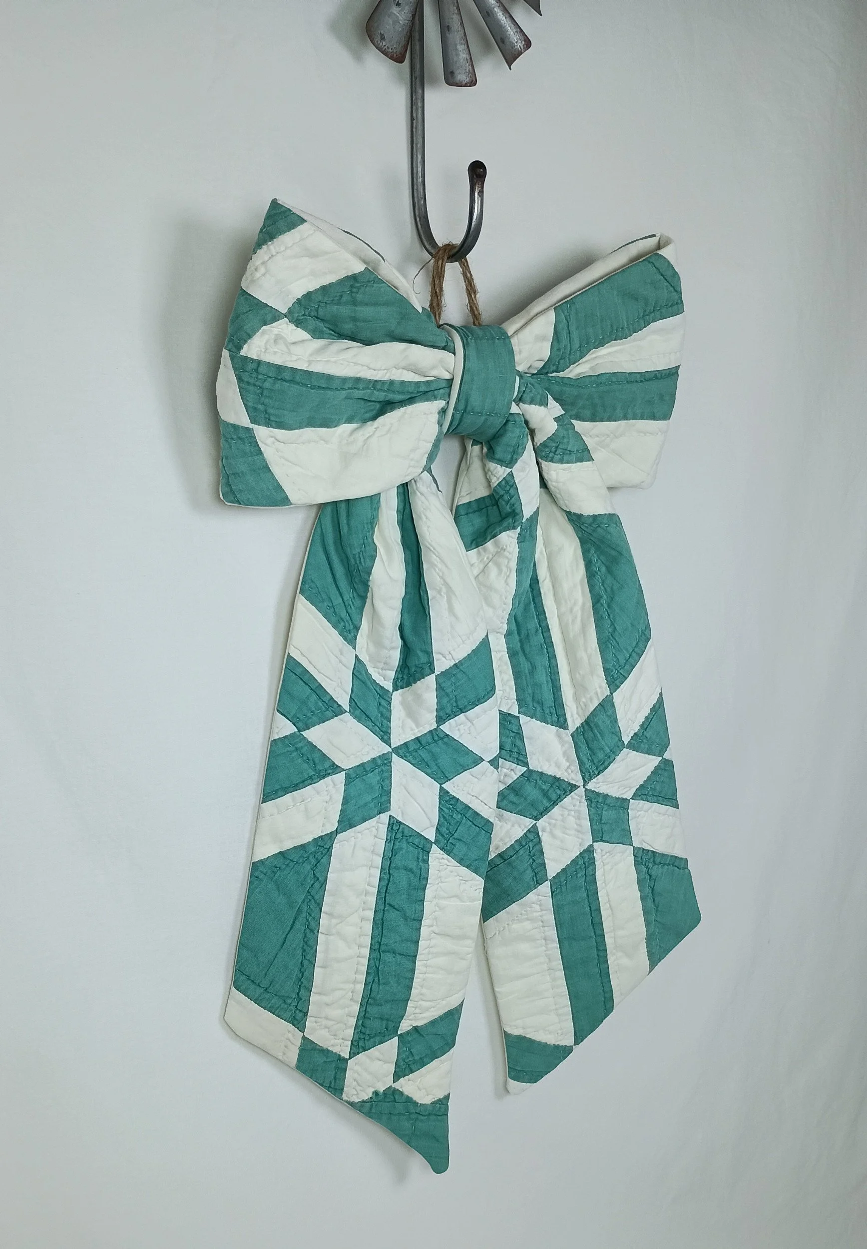 A green and white decorative bow made from an antique quilt