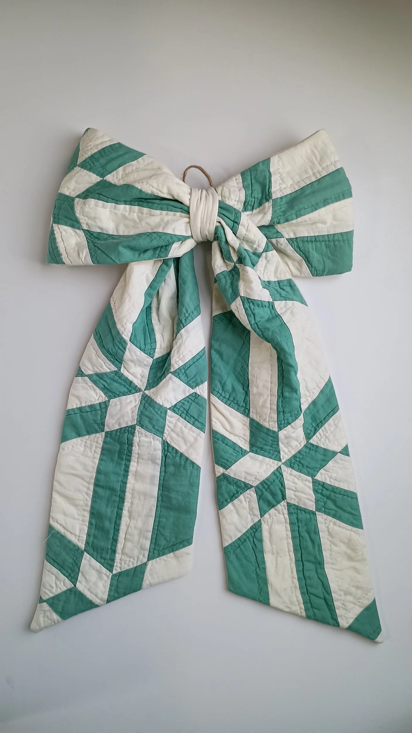 A green and white decorative bow made from an antique quilt