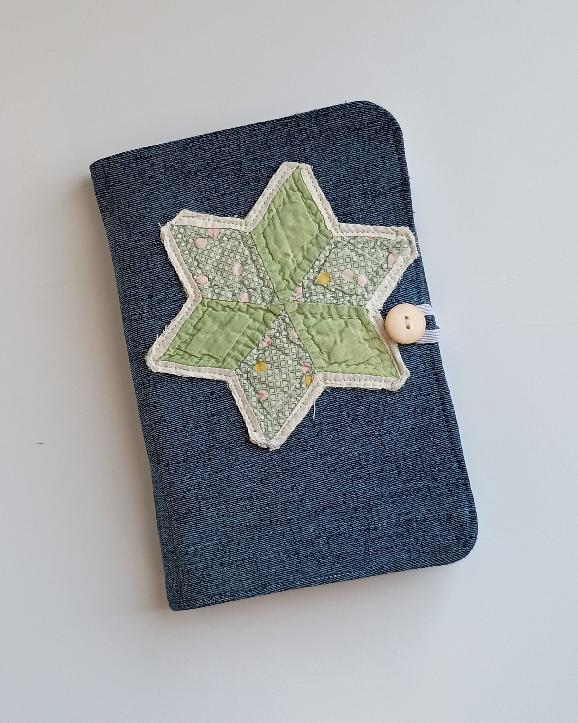A notepad cover made from denim fabric with an antique quilted star on the front and a button closure