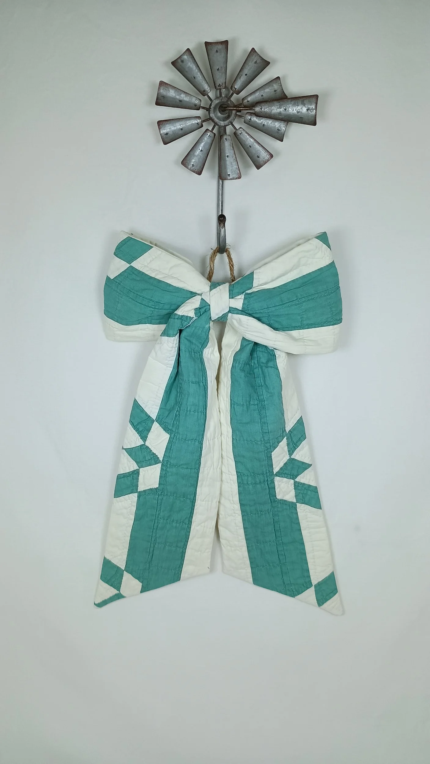 A green and white decorative bow made from an antique quilt