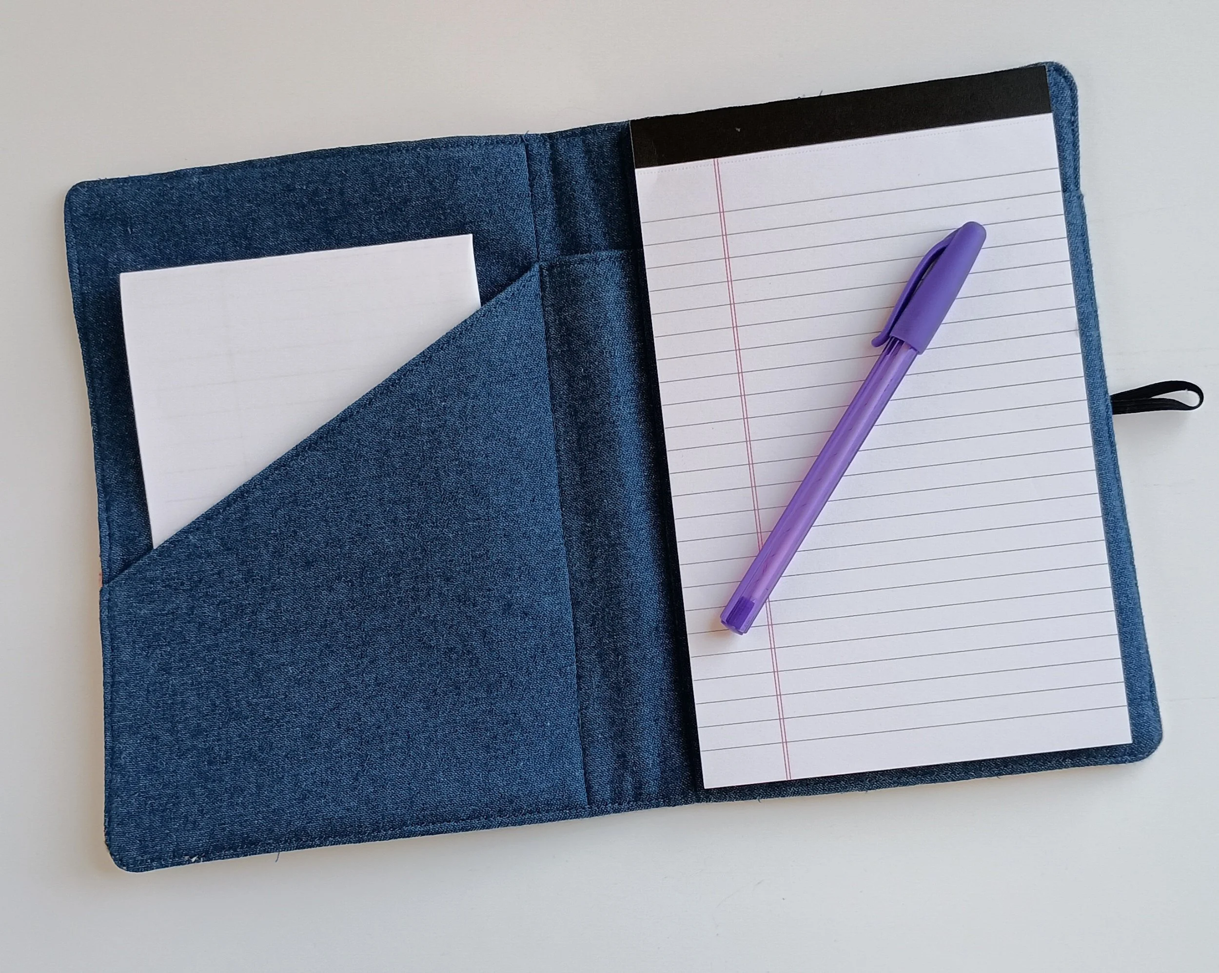 The inside of a notepad cover made with denim fabric, shown with a notepad, pocket, and pen