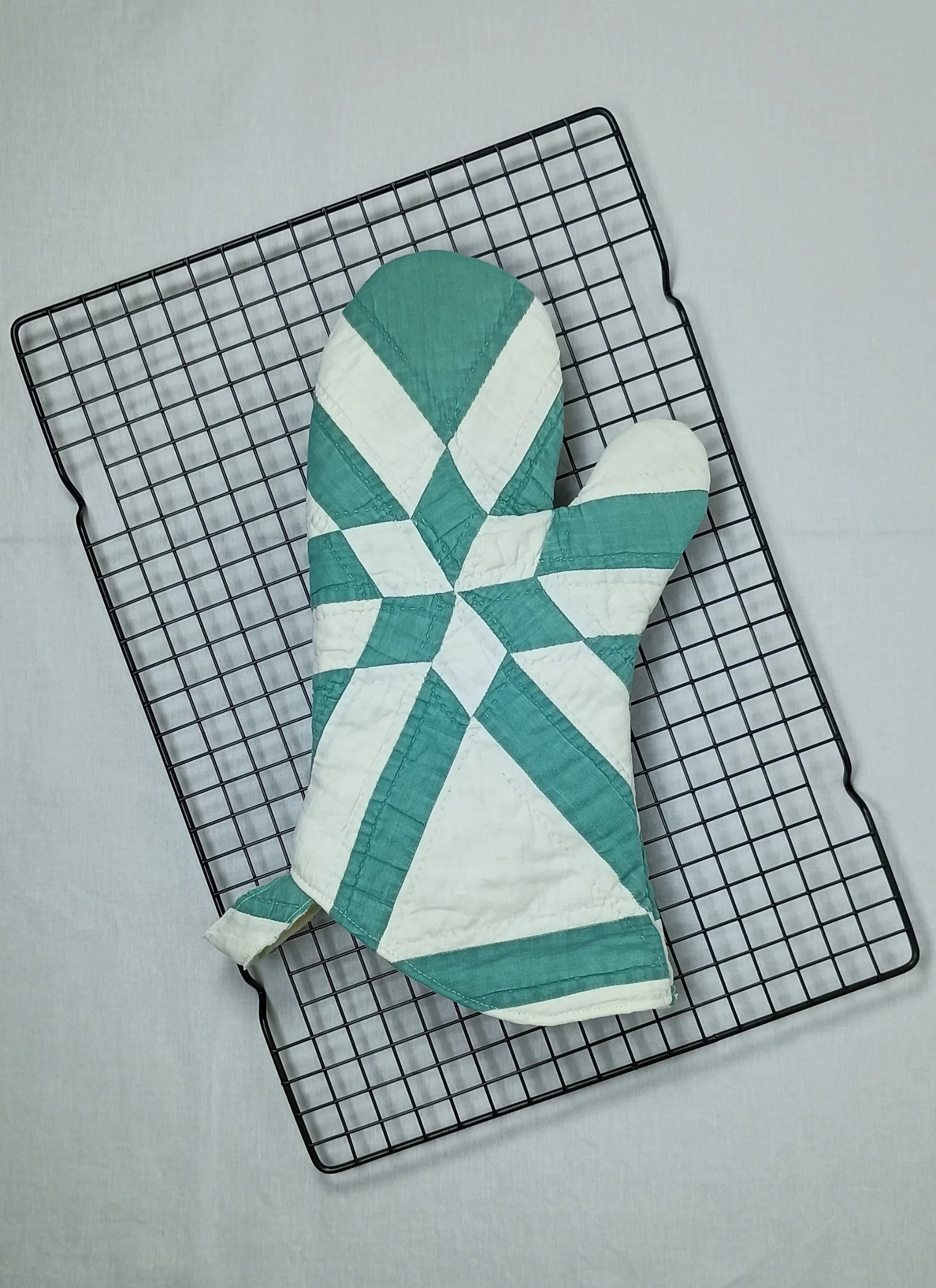 An oven mitt made from a green and white antique quilt with a star pattern