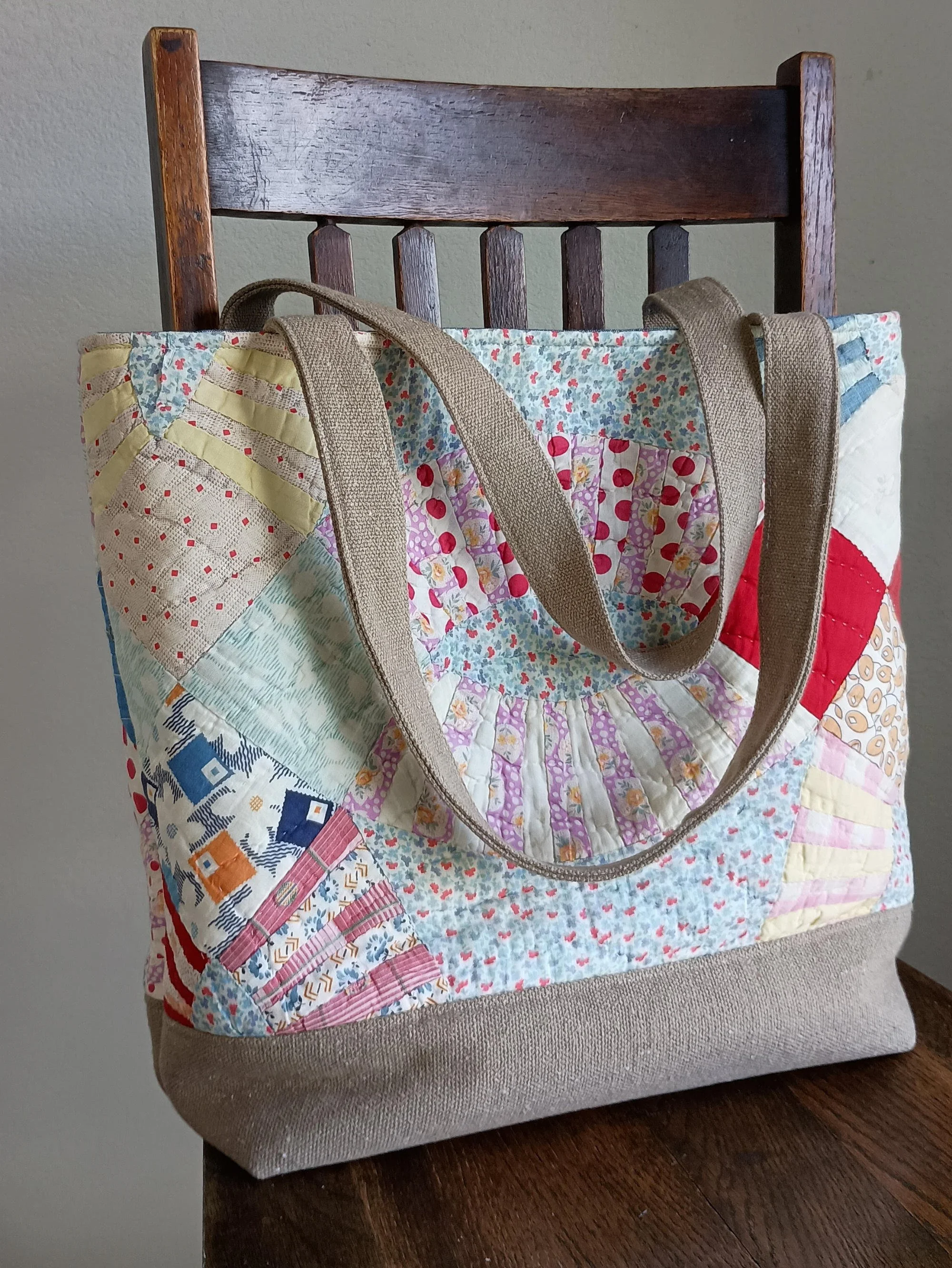 A tote bag made out of an antique quilt sitting on a chair.