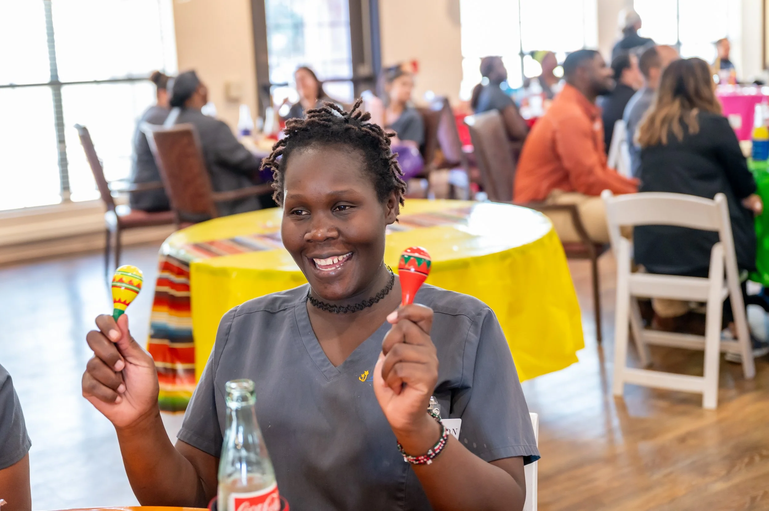 A woman smiling and holding two maracas at a colorful party or celebration.